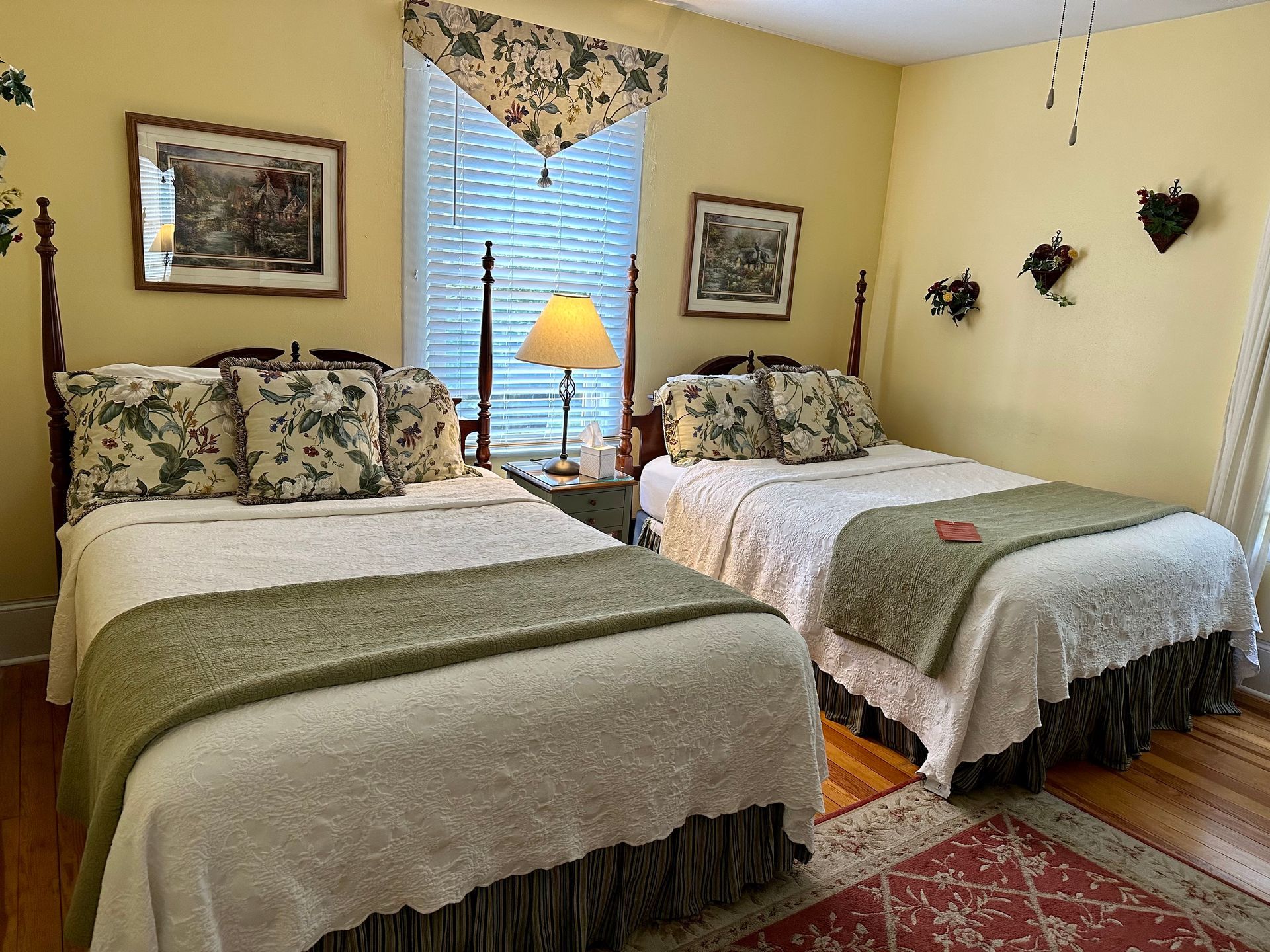 Two twin beds in a yellow bedroom. Each bed has floral pillows and a green and white bedspread.