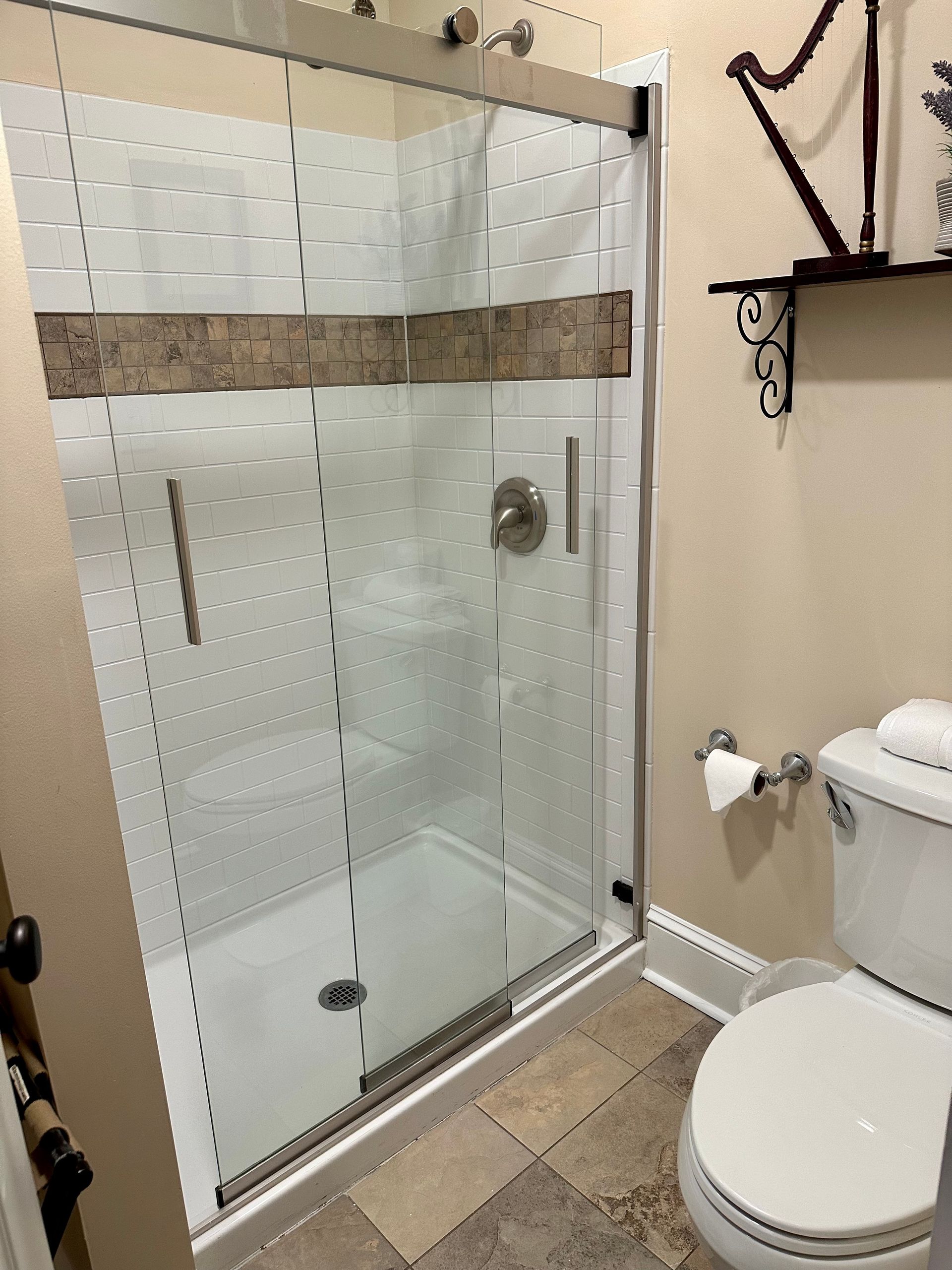 A modern bathroom with a glass shower, a toilet, and a shelf with decorative items. 