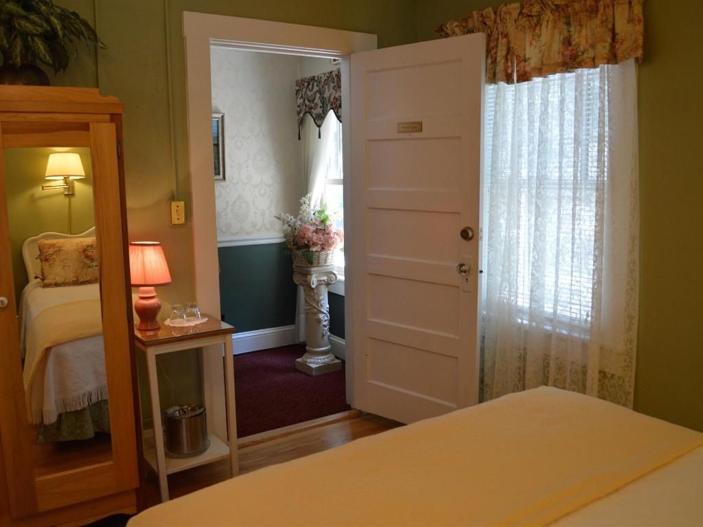 Bedroom with a bed, wardrobe, and doorway to a bathroom. The room has a floral curtain and a lamp on a side table.