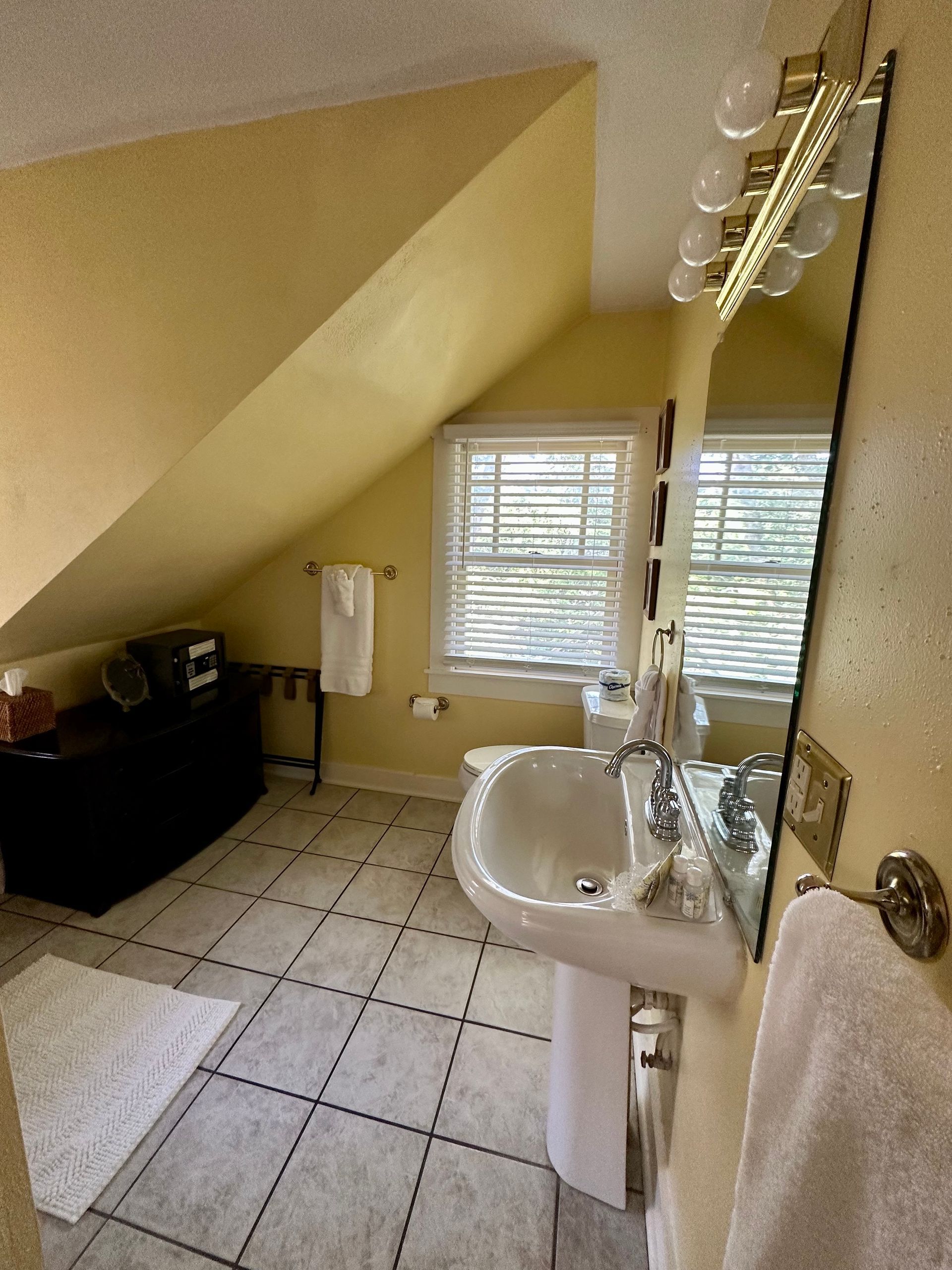 Bathroom with a pedestal sink, long mirror, and black and white tiled floor. 