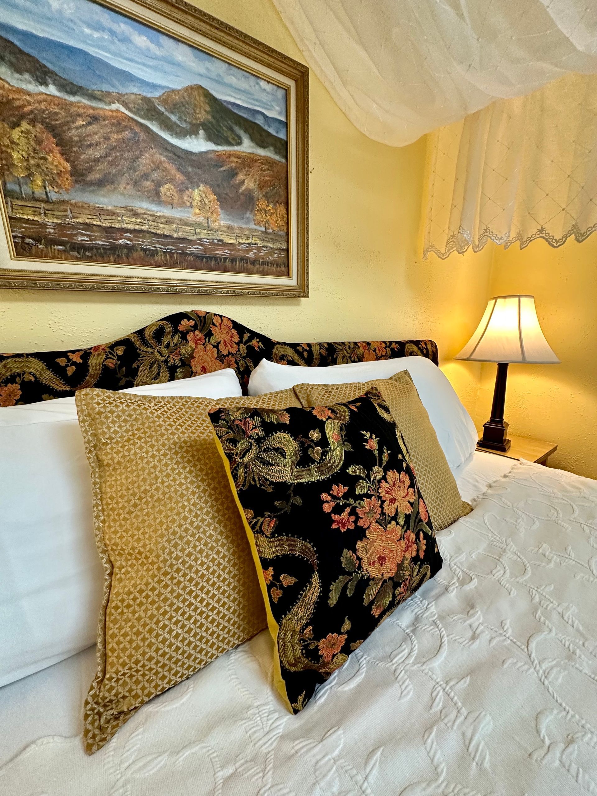 Bedroom with a bed, pillows, and a painting of a landscape on the wall. 