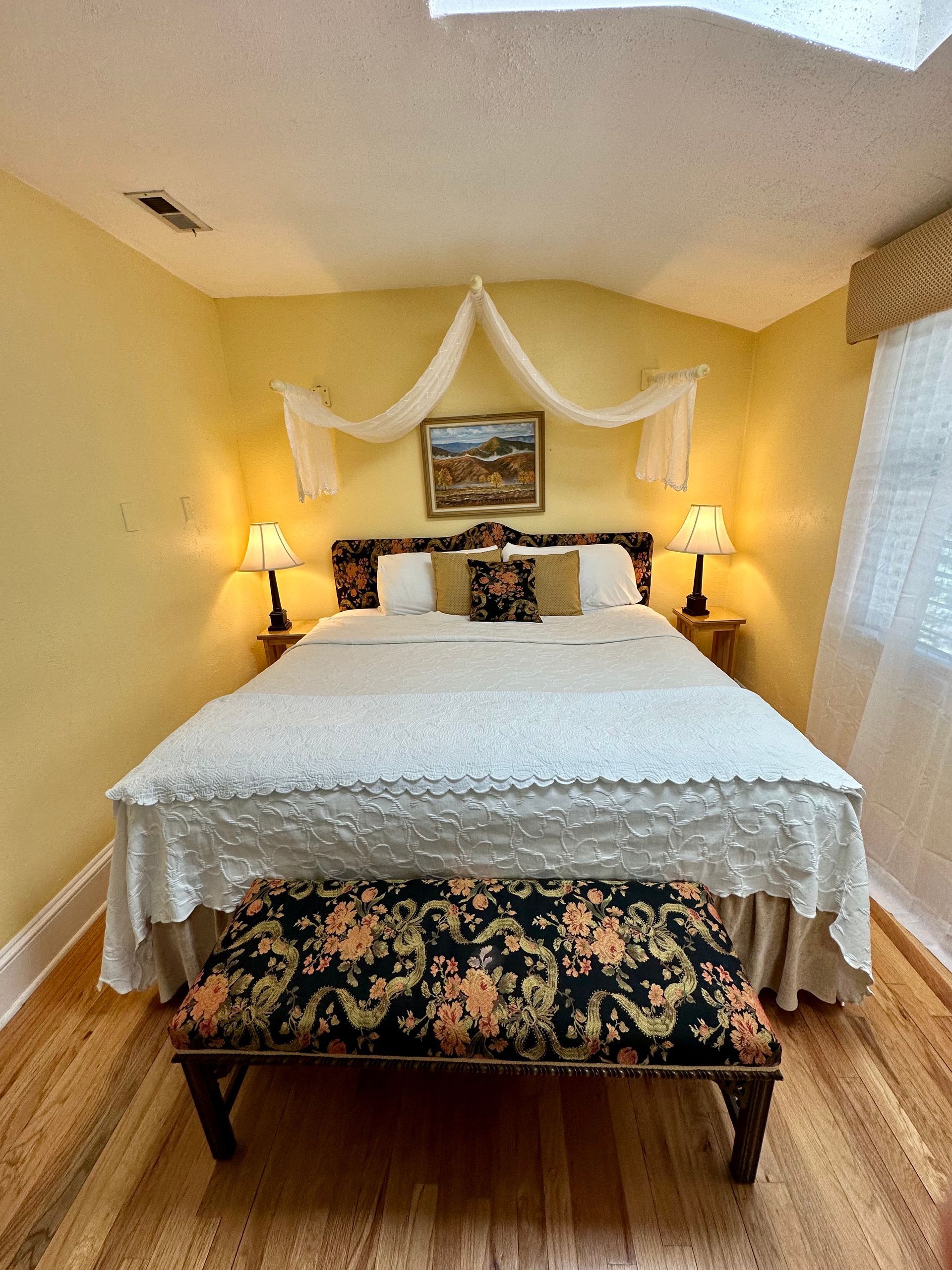 Bedroom with yellow walls, hardwood floors, and a bed covered with a white patterned bedspread. 
