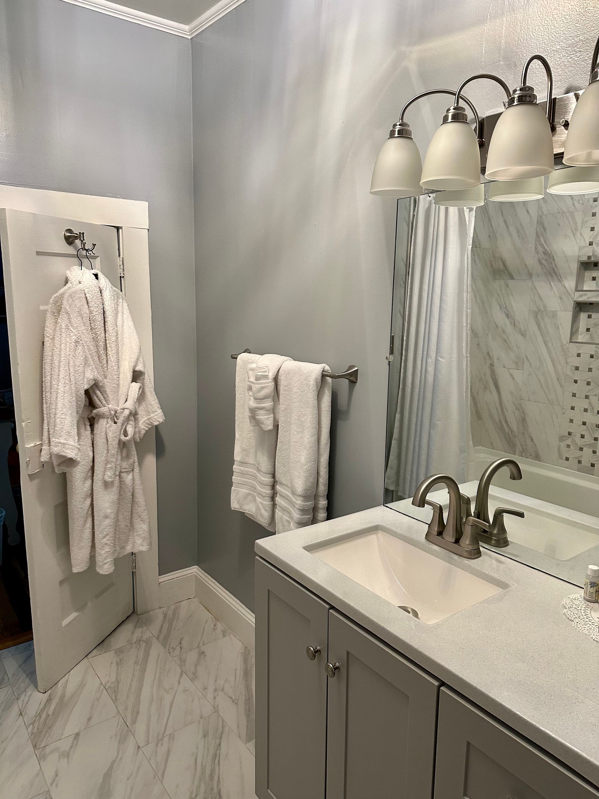 Bathroom with gray walls, a vanity, and a white robe hanging on the door. White towels are on a towel bar.