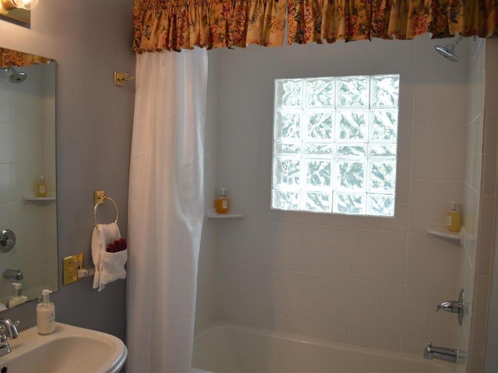 Bathroom with a bathtub, shower curtain, and a window made of glass blocks. A floral valance hangs above.