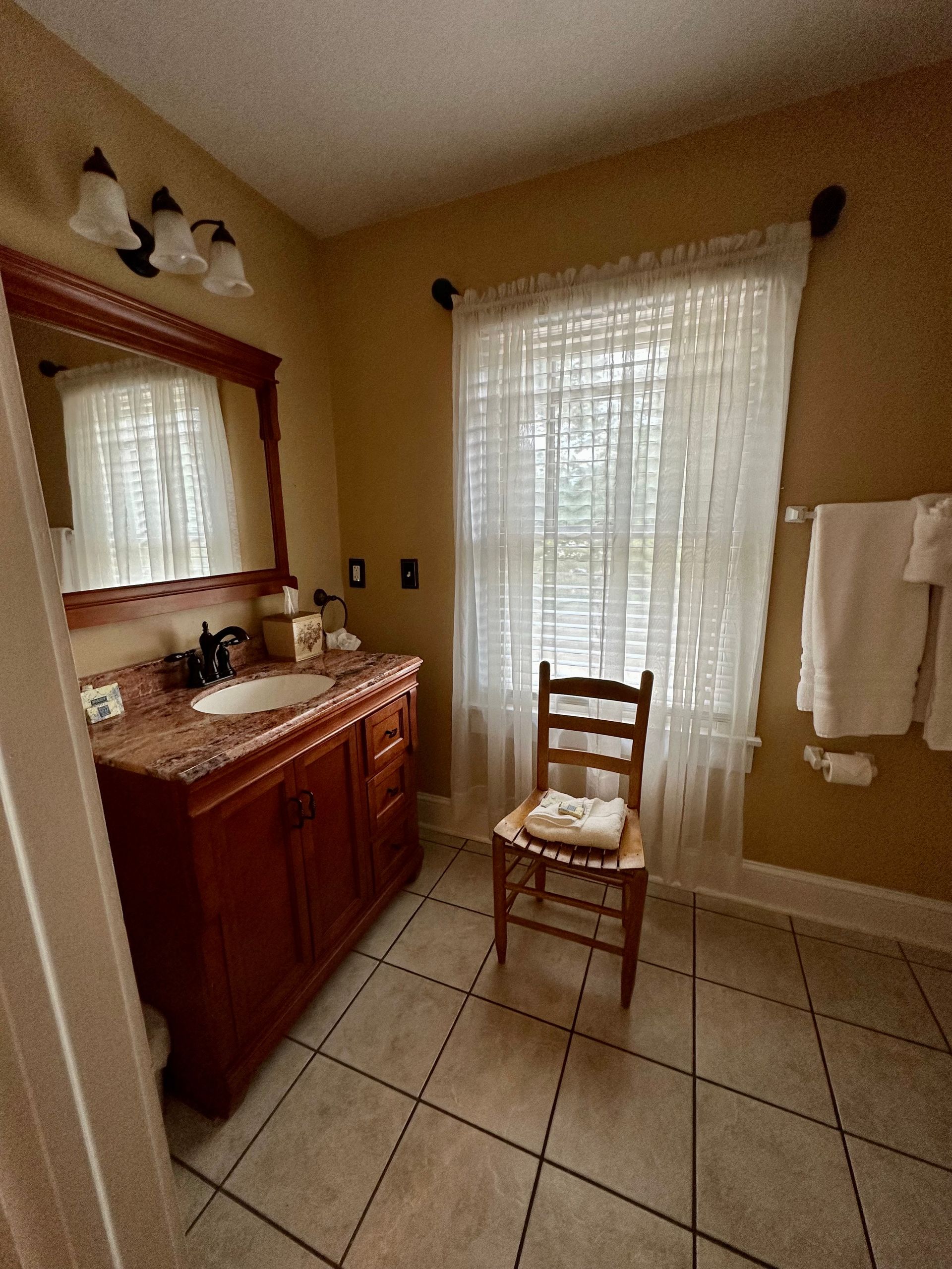 Bathroom with a vanity, window, and a chair. The walls are beige, and the vanity is wooden with a red countertop.