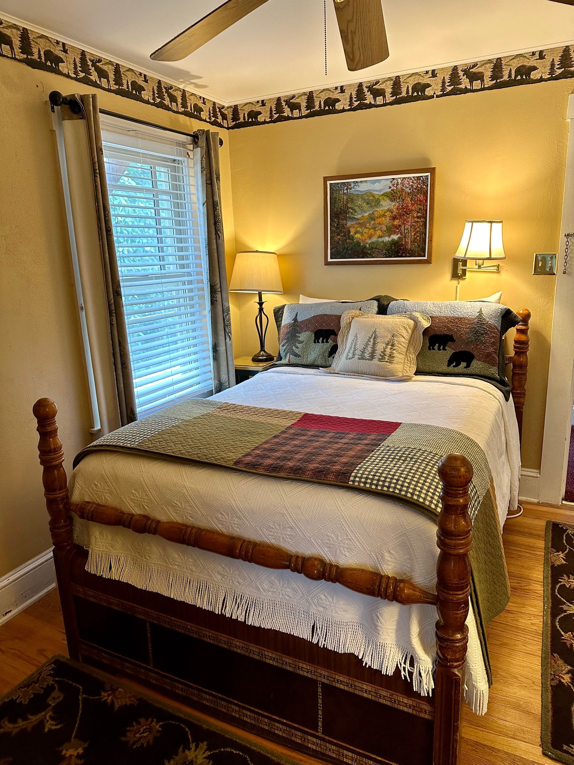 Bedroom with a wooden bed, decorative pillows, and a quilt.  The walls are yellow with a forest animal border.