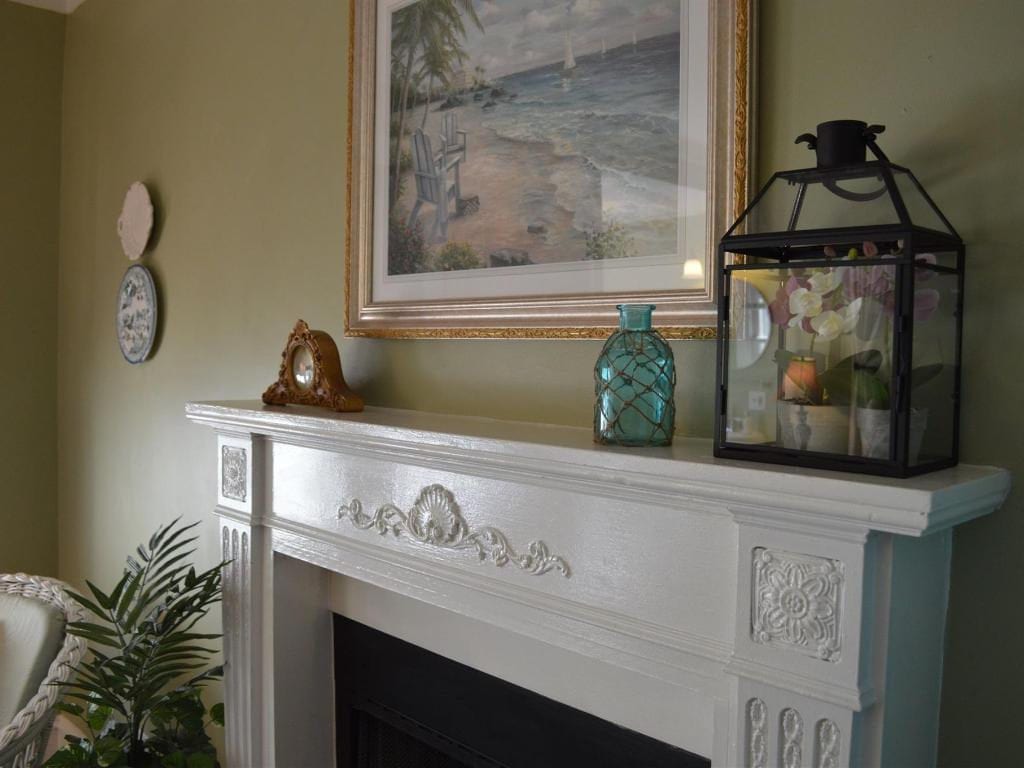White fireplace mantel with framed art, teal glass vase, and decorative lantern. 