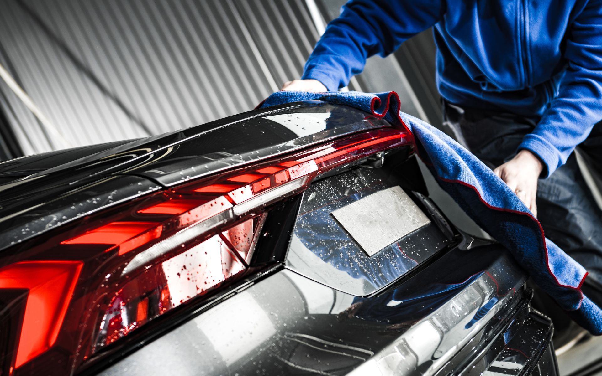 Person drying a black car with a blue cloth at a car wash, with red taillights.
