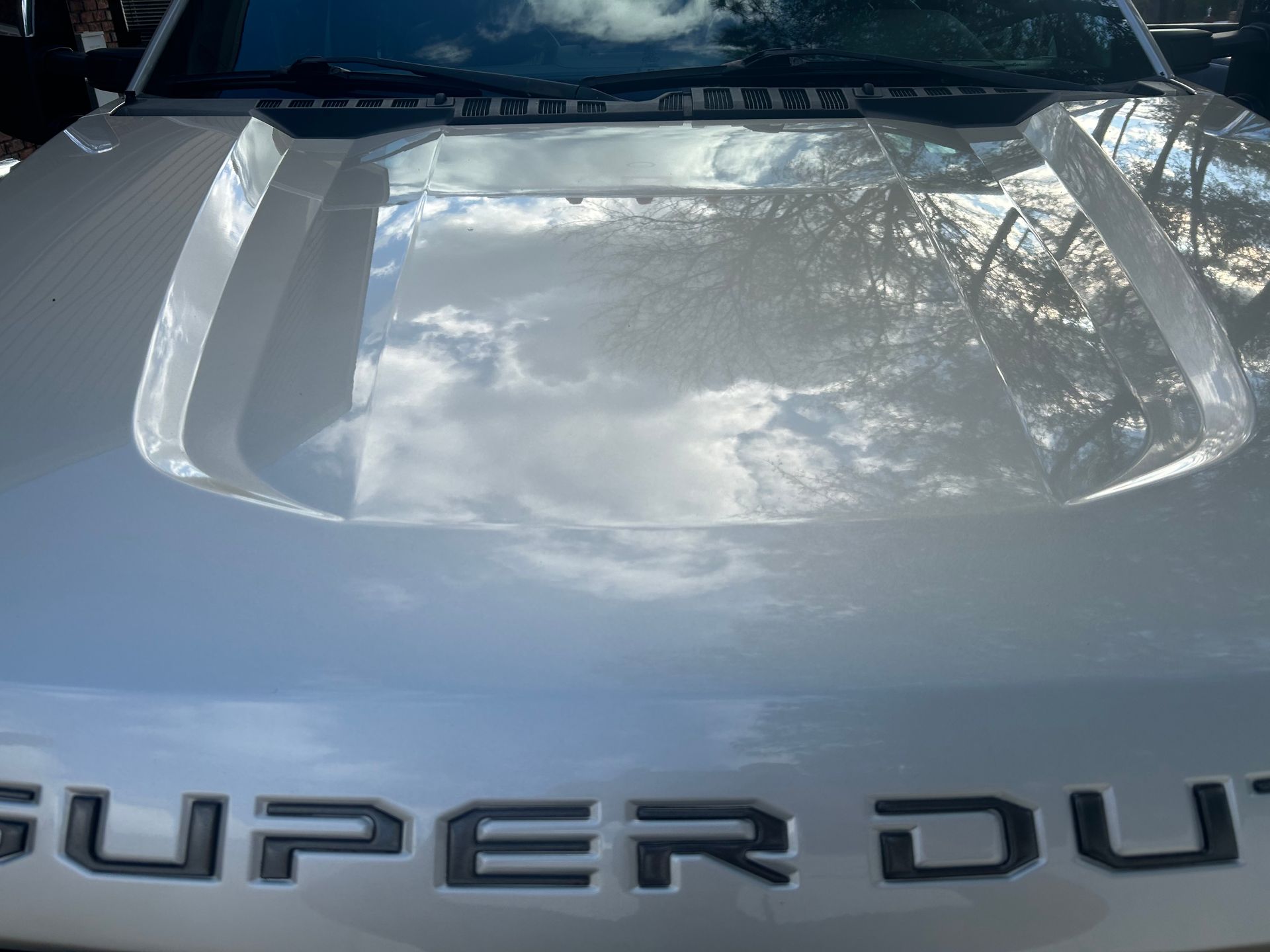 Silver truck hood reflecting a cloudy sky; the word