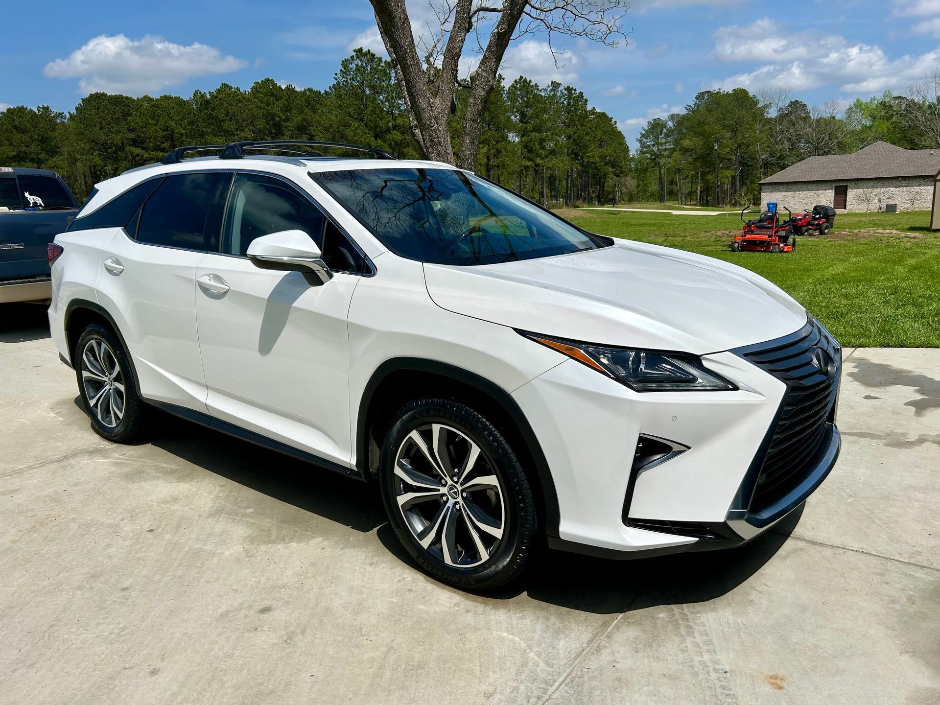 White Lexus SUV parked on a concrete driveway. Trees and a house are in the background.