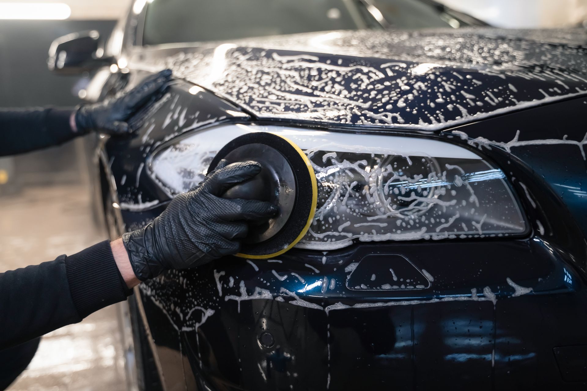 Hands washing a black car, using a buffing tool.