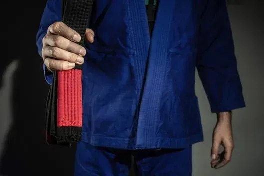 A jiu jitsu practitioner holding a black belt with a red stripe.