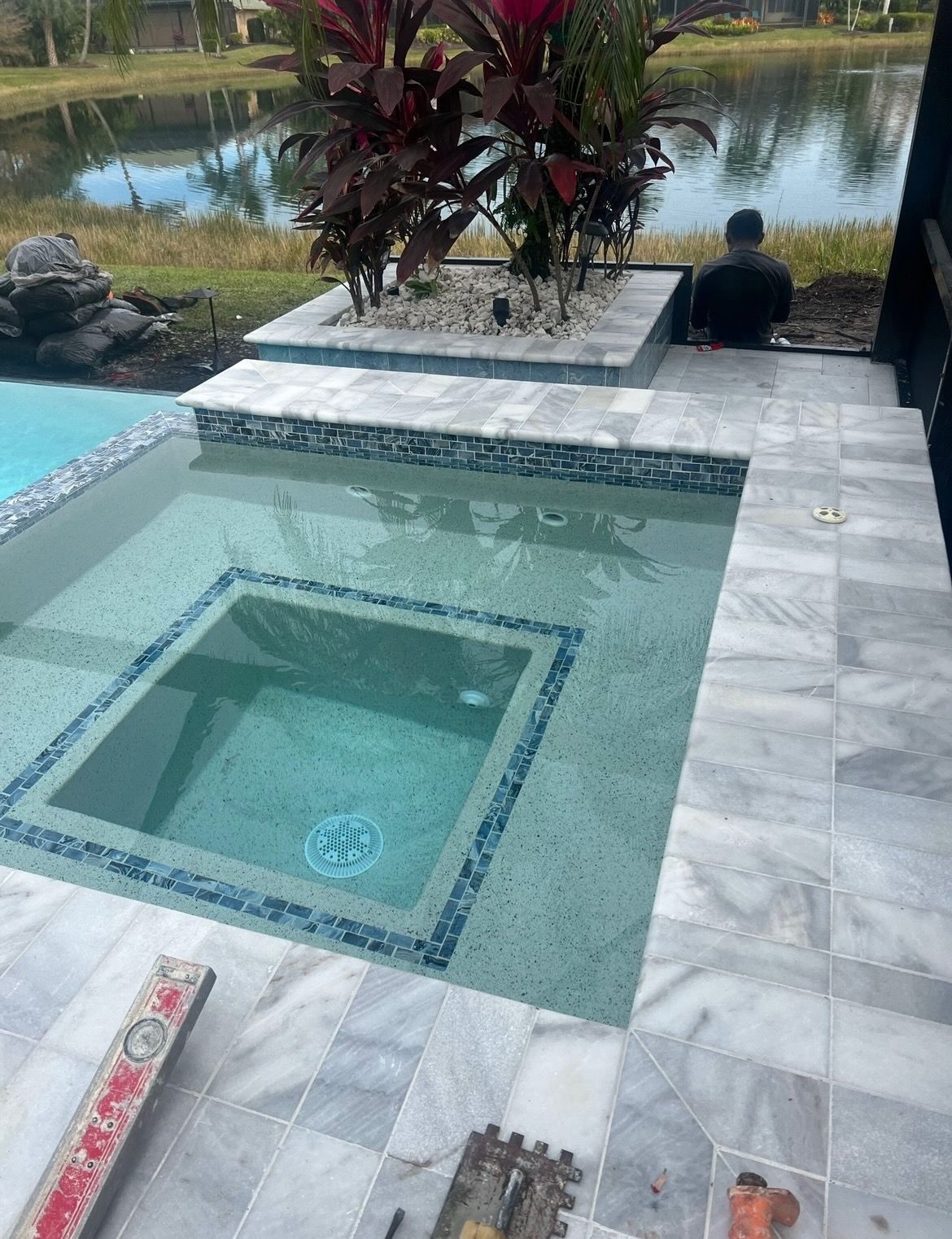 A man is sitting on a patio next to a swimming pool.