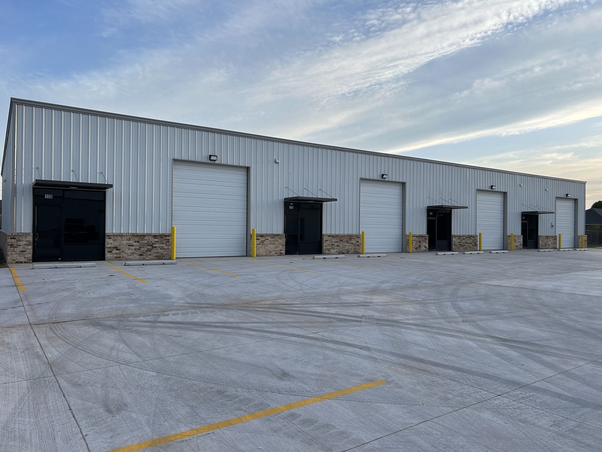 Large gray metal warehouse building with five overhead doors and paved parking area.
