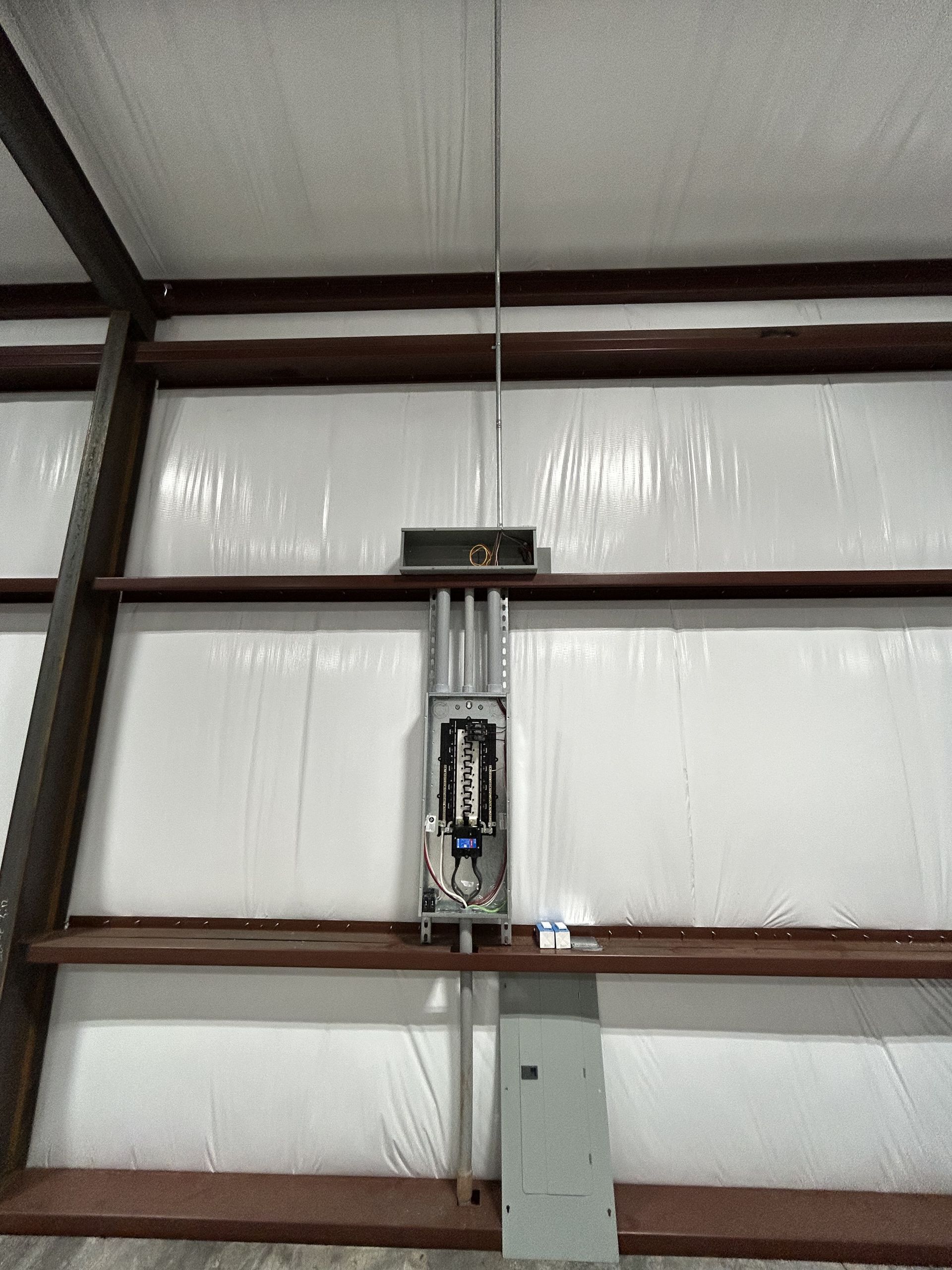 Electrical panel, conduit, and lightning rod installed on a white-walled interior with brown support beams.