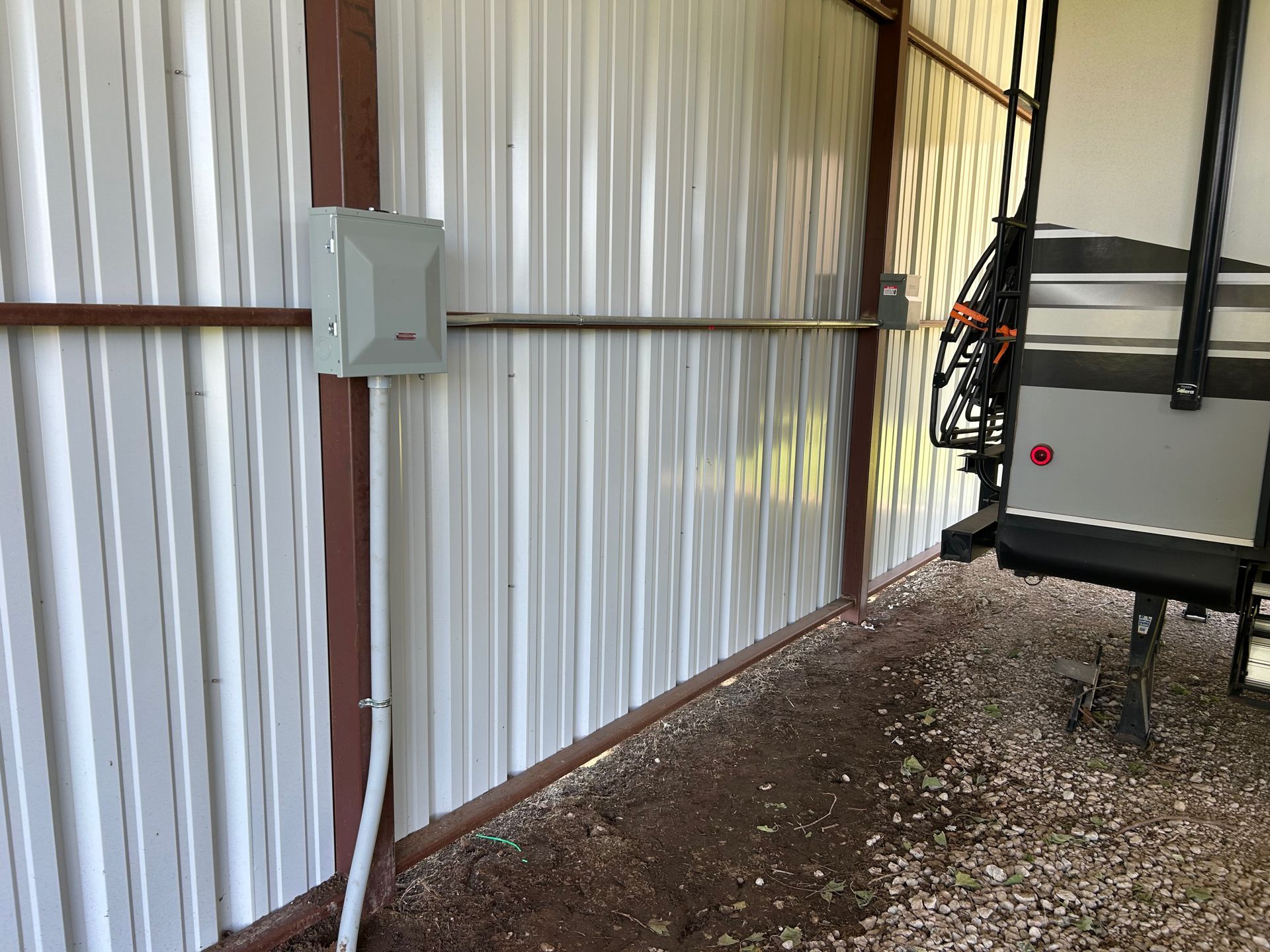 Gray electrical box and conduit on a corrugated metal shed wall near an RV.
