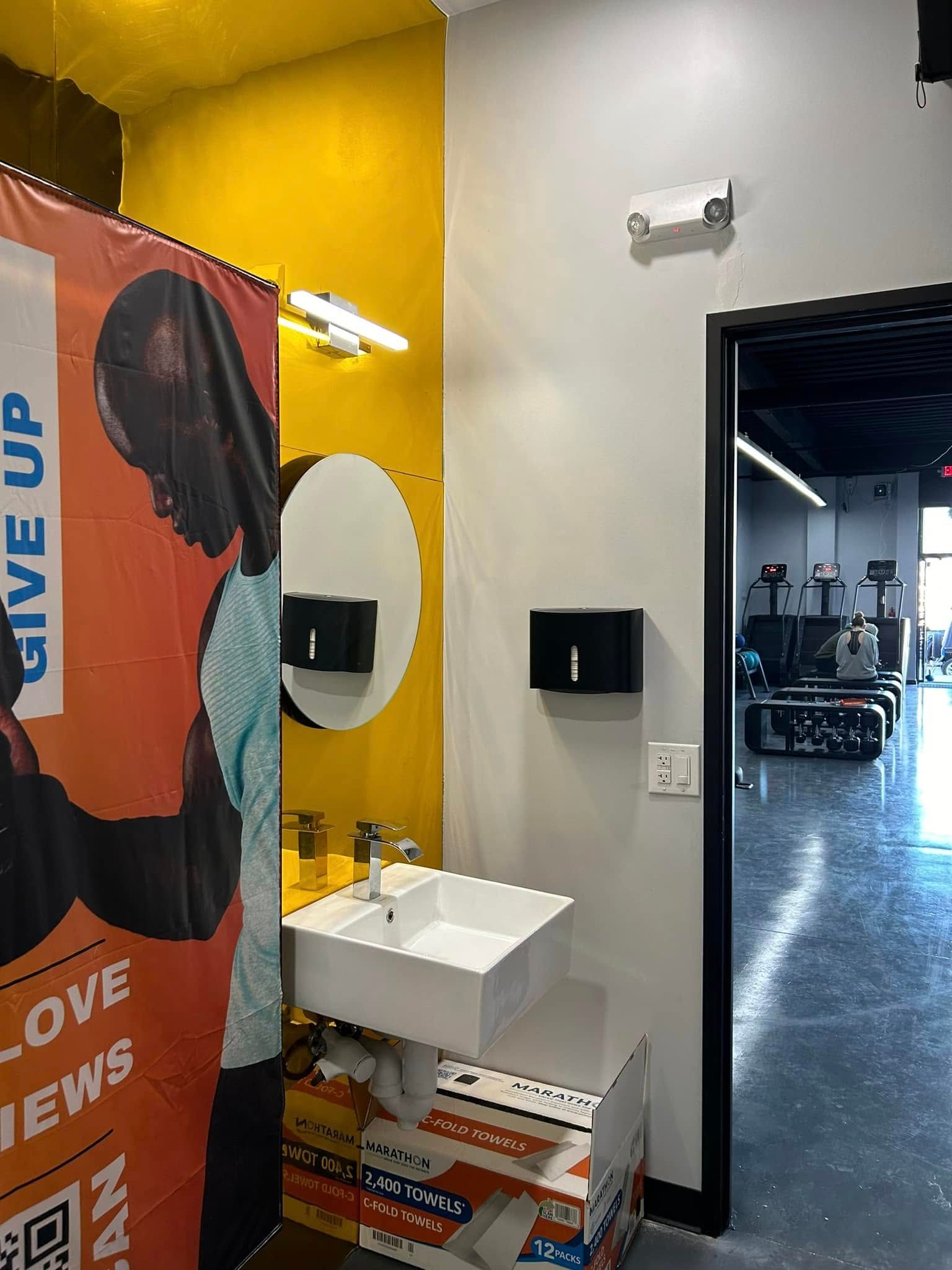 A white sink and mirror next to a doorway in a gym, with a banner to the left.