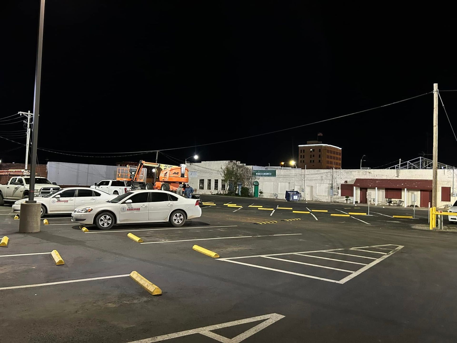 Parking lot at night with cars parked and a building in the background.