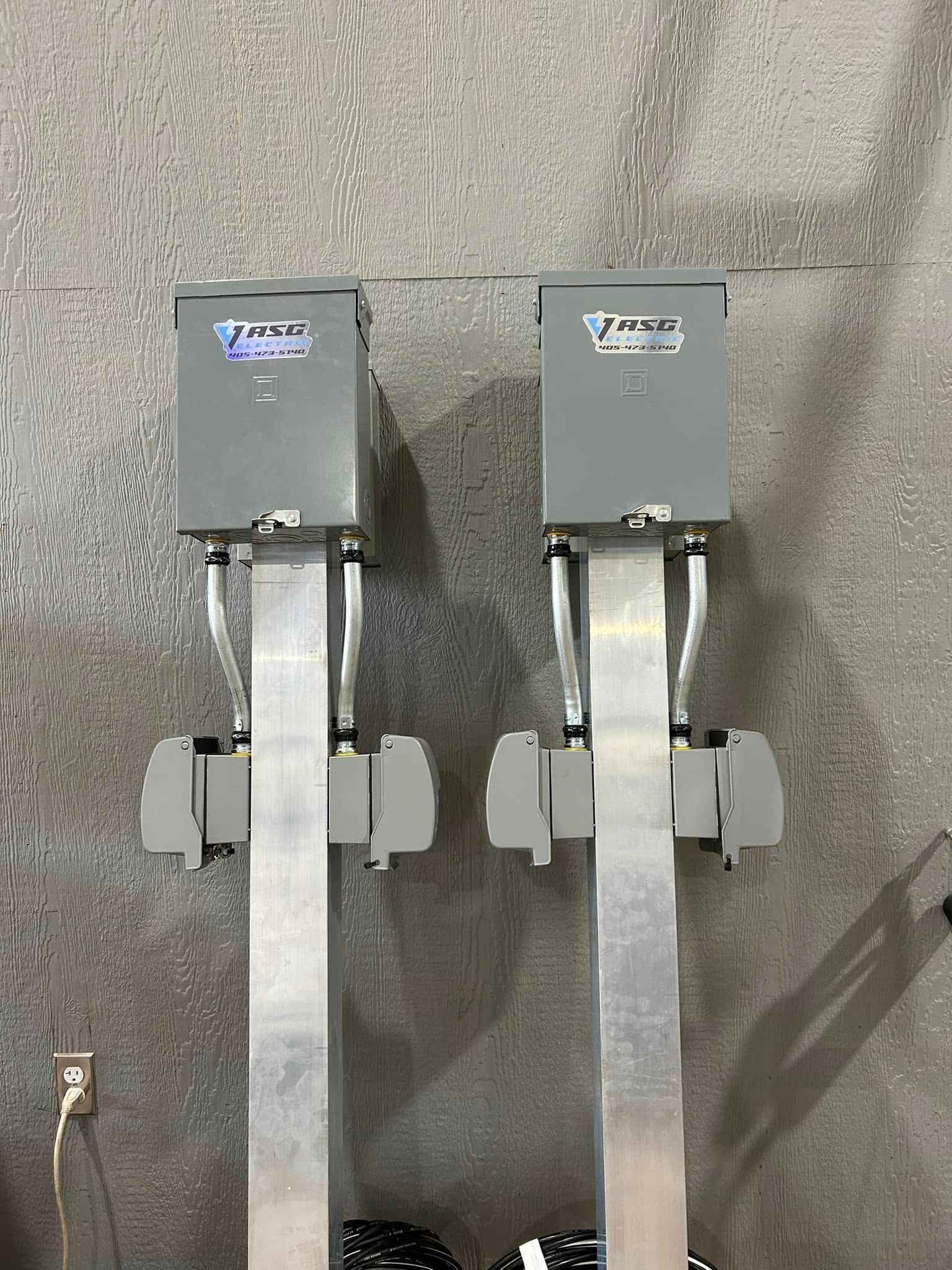 Two gray electrical boxes mounted on silver metal poles, gray wall background.