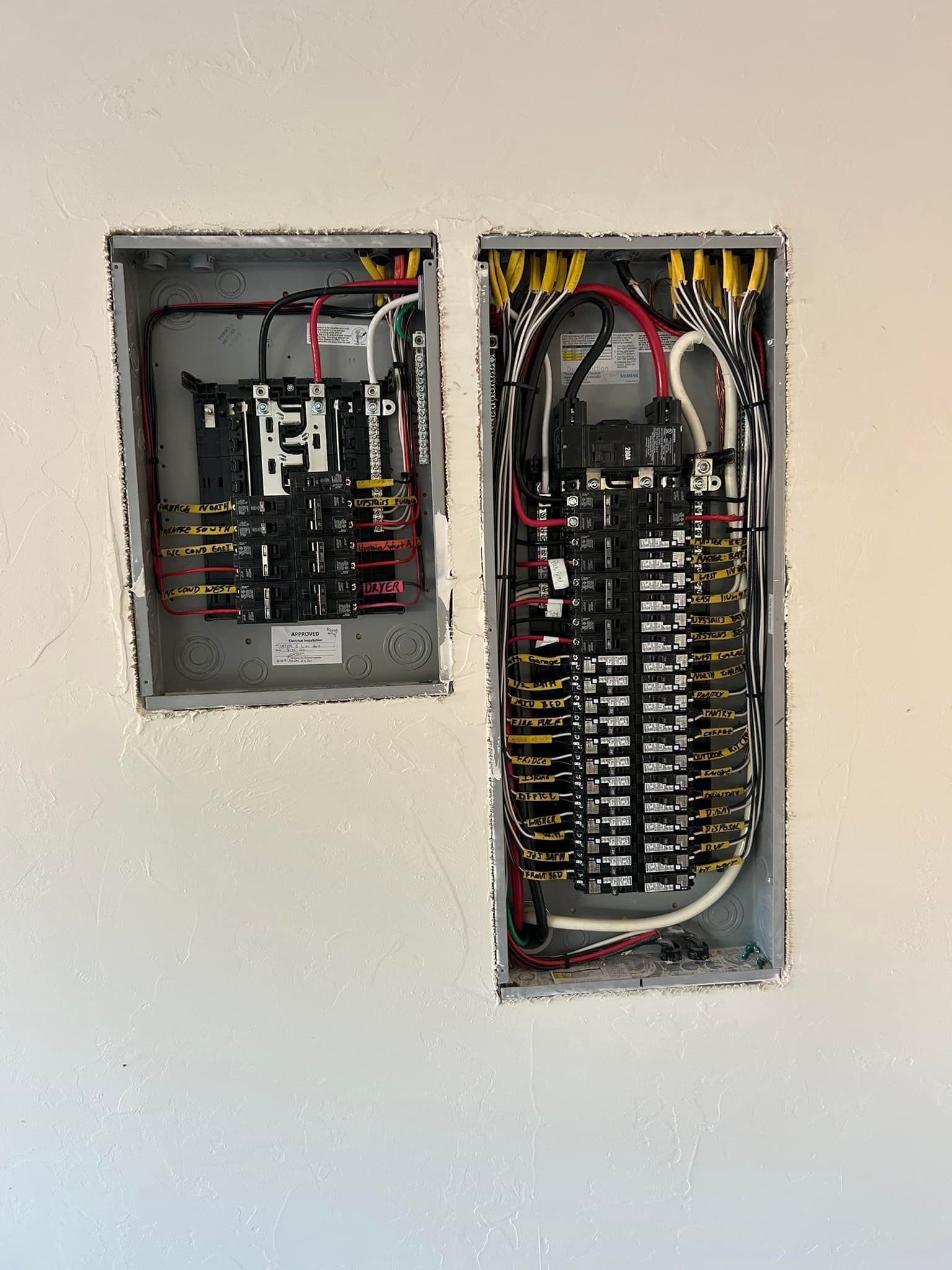 Two electrical panels installed in a white wall; wiring visible inside.