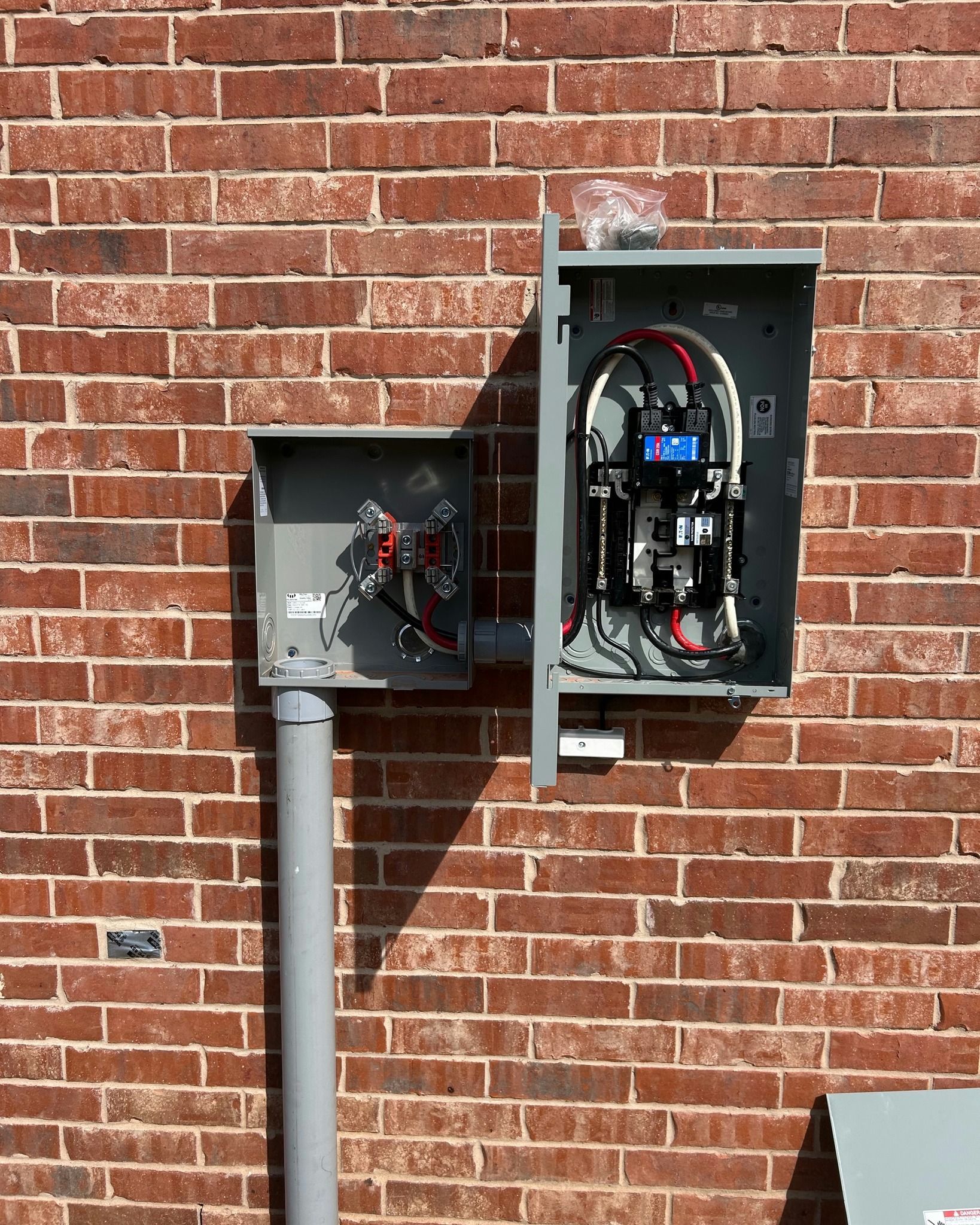 Outdoor electrical panel on a brick wall, with open boxes and wiring visible.