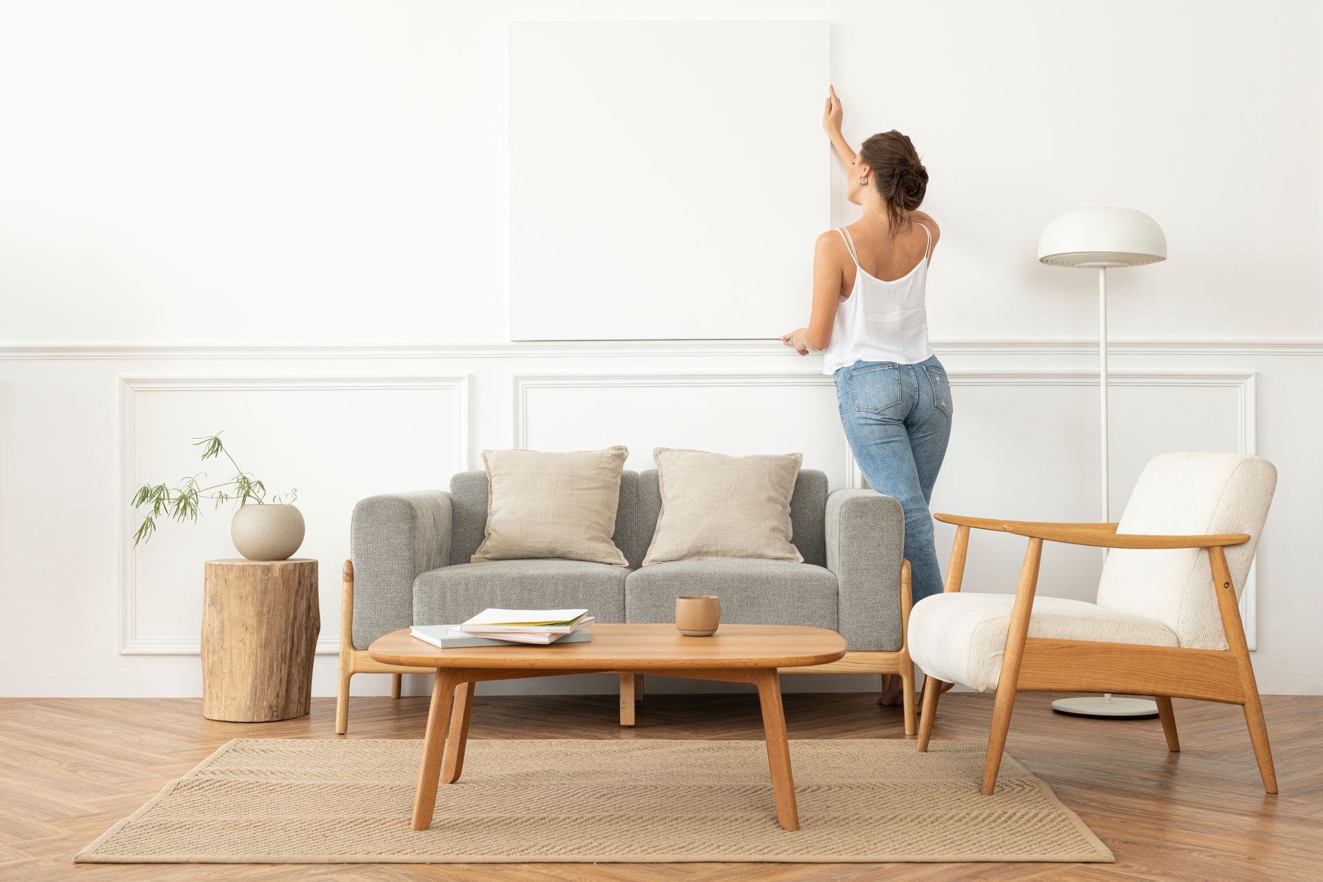 A woman is hanging a picture on a wall in a living room.