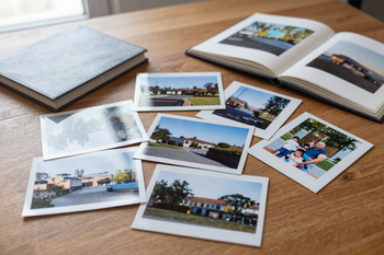 Fotos impresas esparcidas sobre una mesa de madera, junto a un álbum de fotos abierto y un cuaderno gris