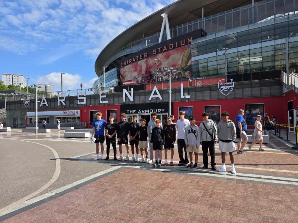 Group of people pose in front of Emirates Stadium, Arsenal Football Club.
