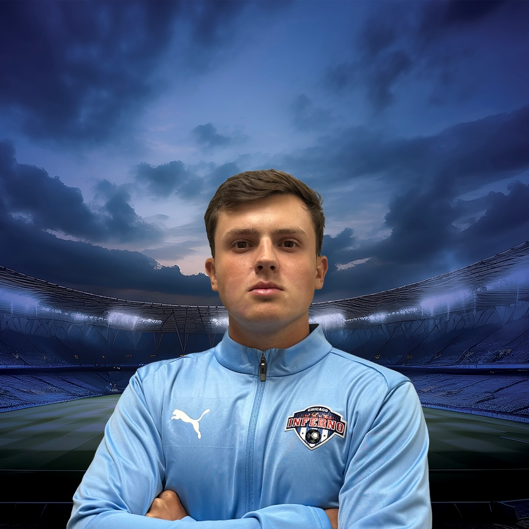 Coach Bruno Tonini in light blue jacket with arms crossed, in front of a stadium background.