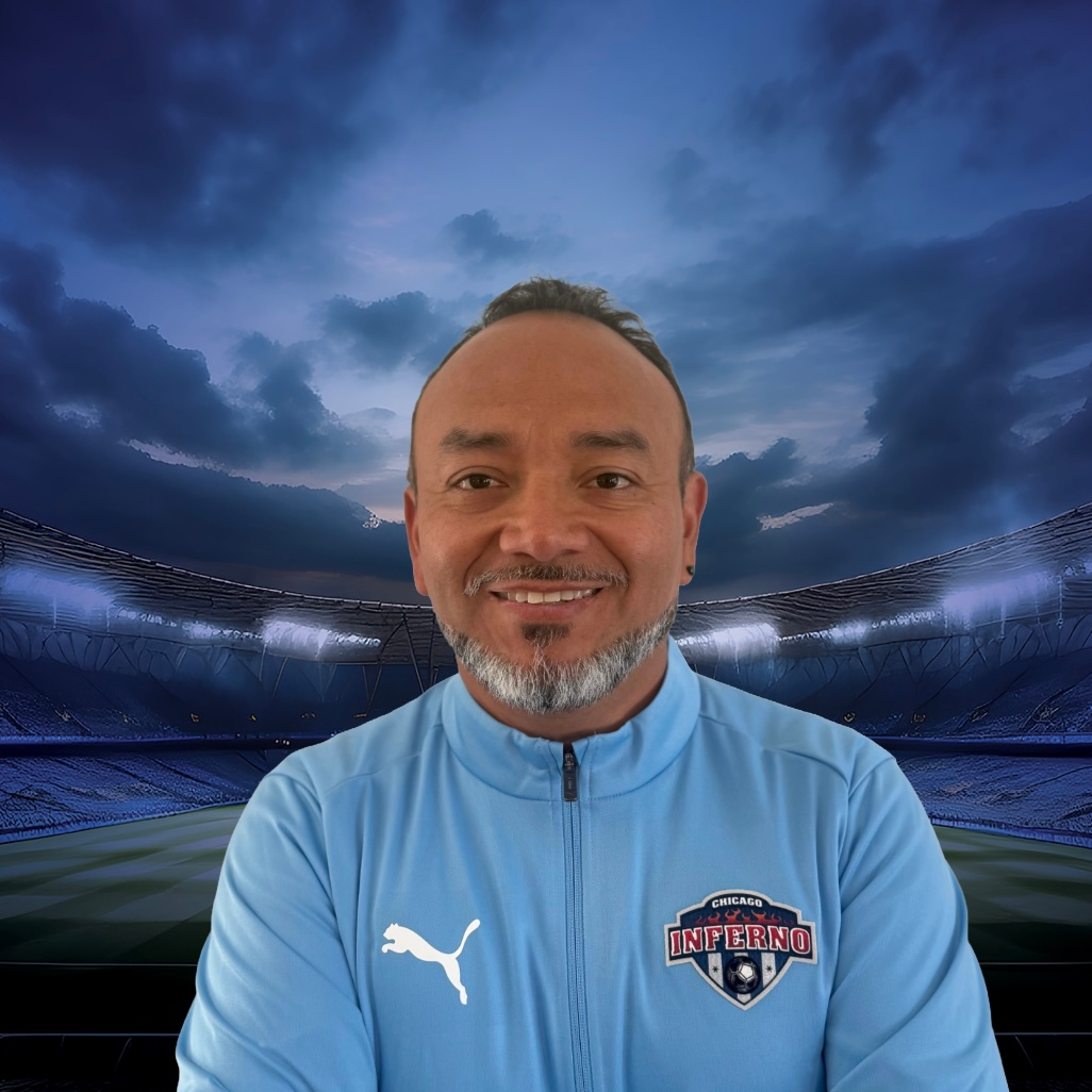Coach Paul Tafur in light blue jacket smiling, in front of a stadium background.