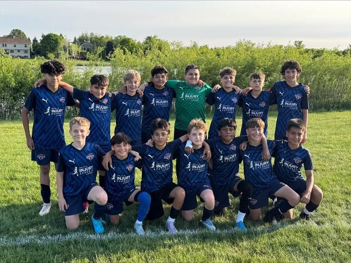 Soccer team posing for a group photo on a grass field, wearing navy blue jerseys.