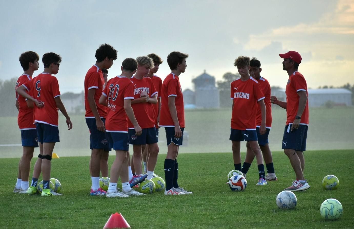 Soccer players in red shirts and blue shorts listen to coach on green field.