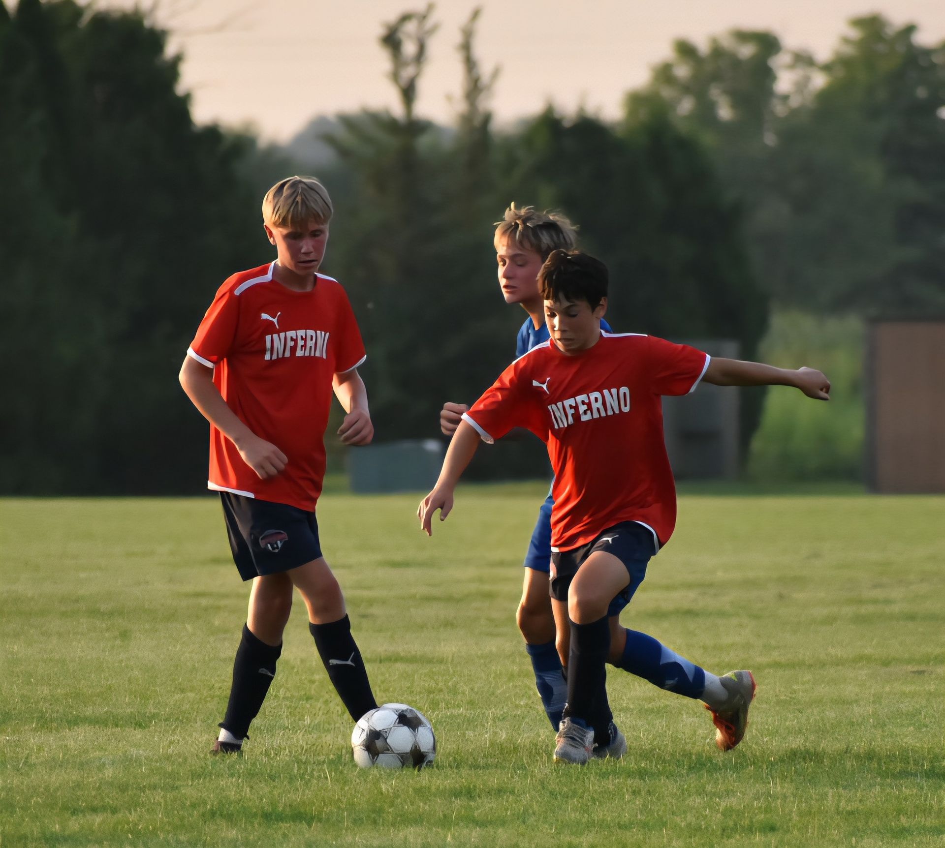 Soccer players in red jerseys and blue shorts on a green field, one dribbling, others nearby.