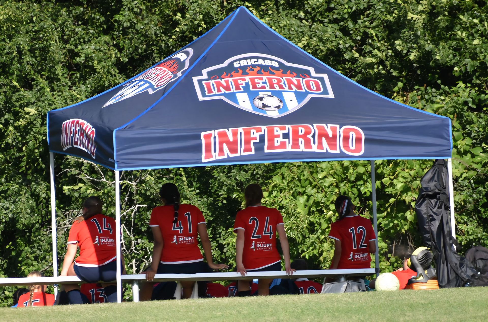 Soccer players in red jerseys seated under a blue