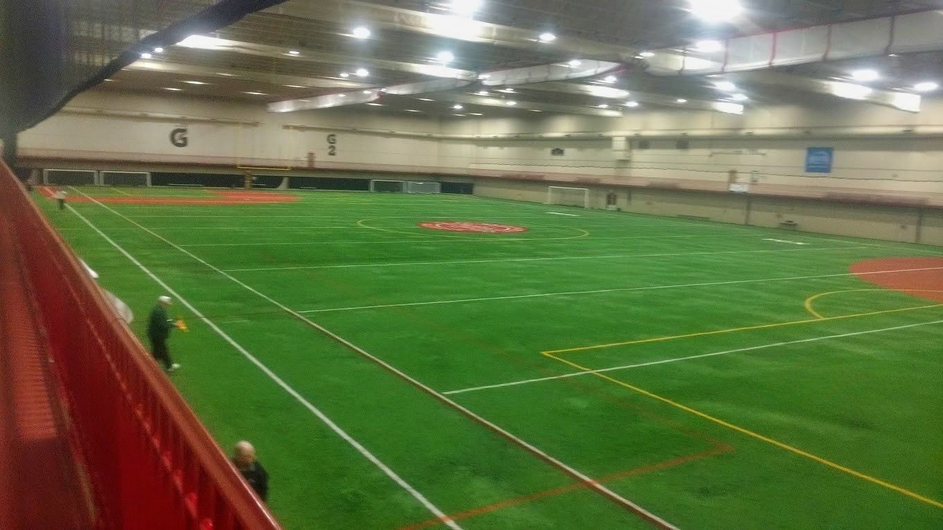Indoor sports field with green turf, white lines, and a red track.