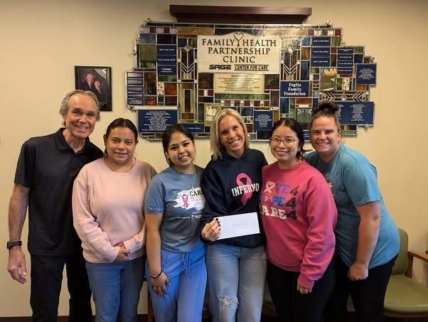 Group smiles in front of a clinic sign. Holding a check, a woman is surrounded by others.