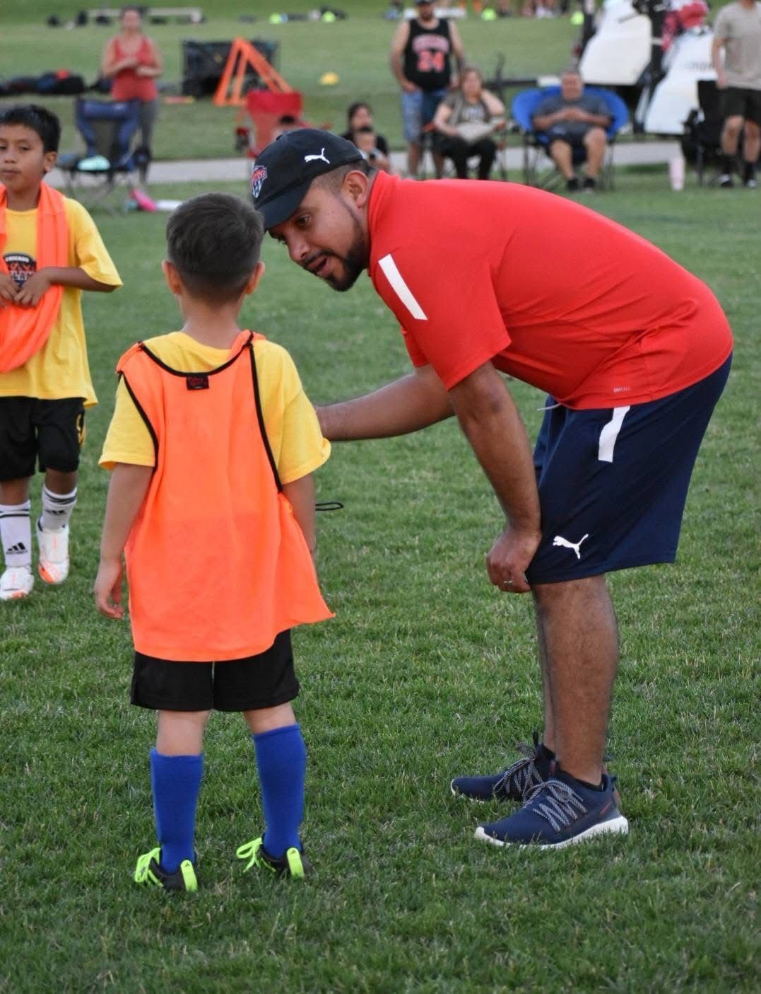 Coach talking to a young soccer player on a grassy field. Both are wearing sports attire.