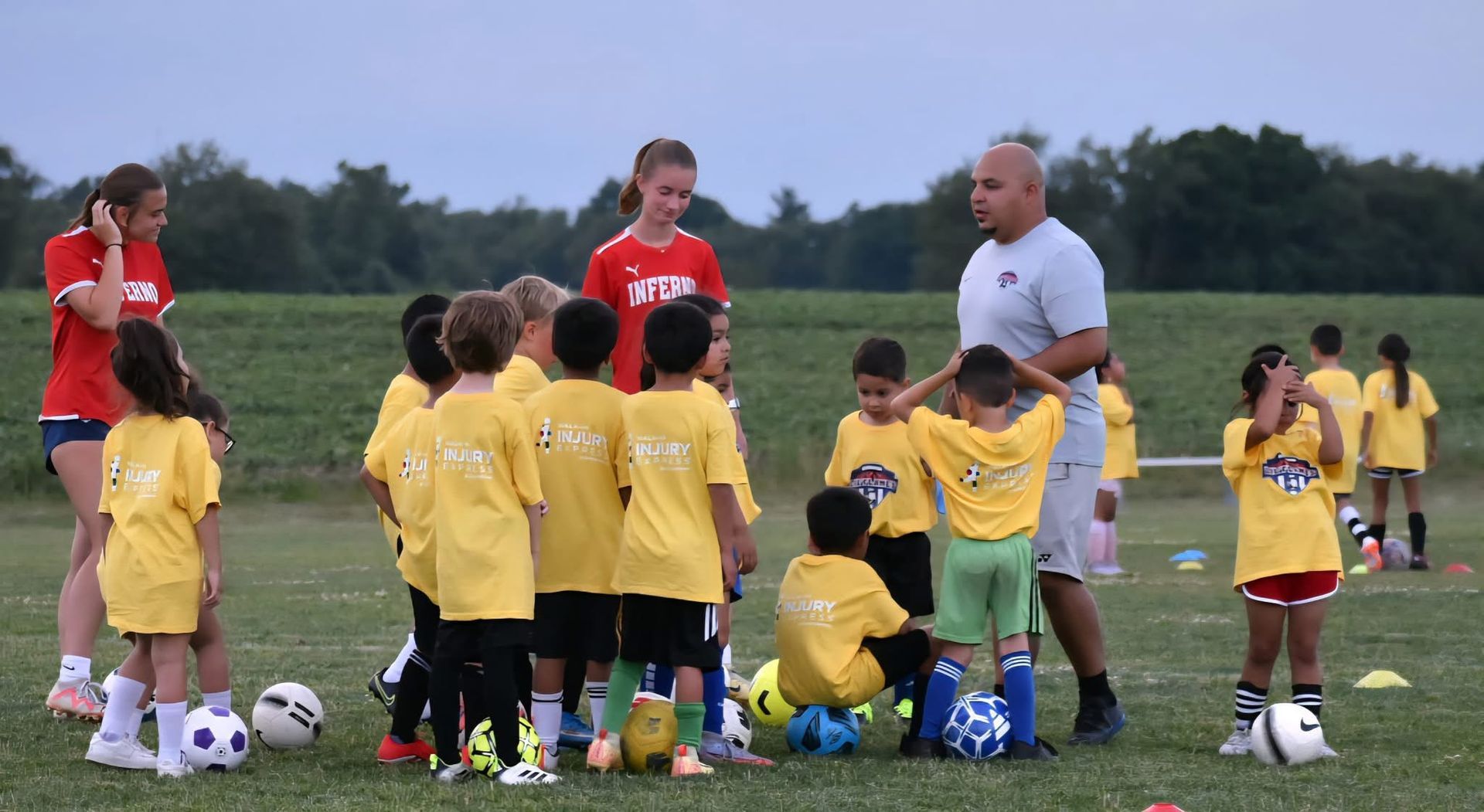 Soccer coach with young players on a field; they wear yellow shirts.