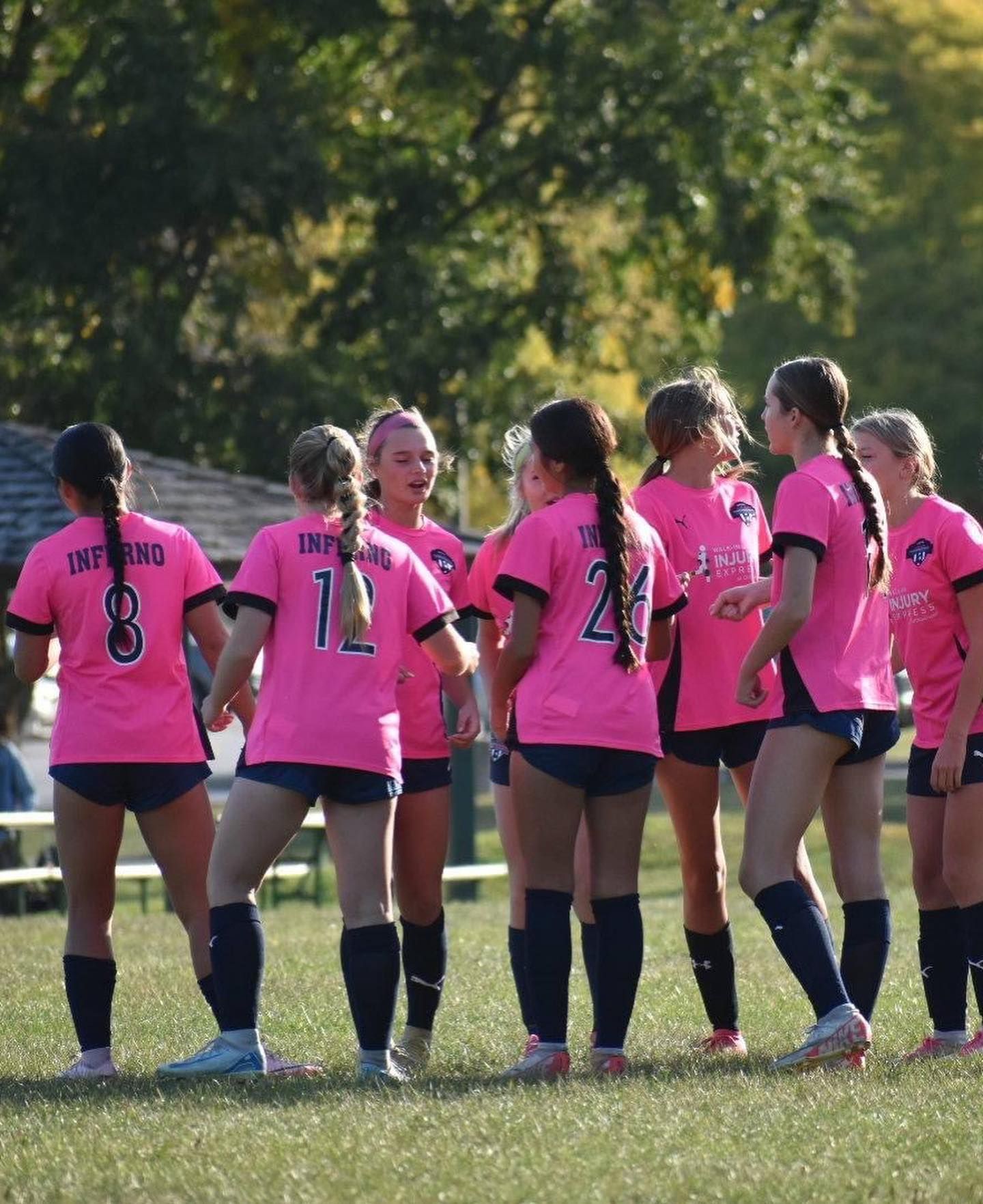 Soccer players in pink jerseys celebrate on a grassy field.