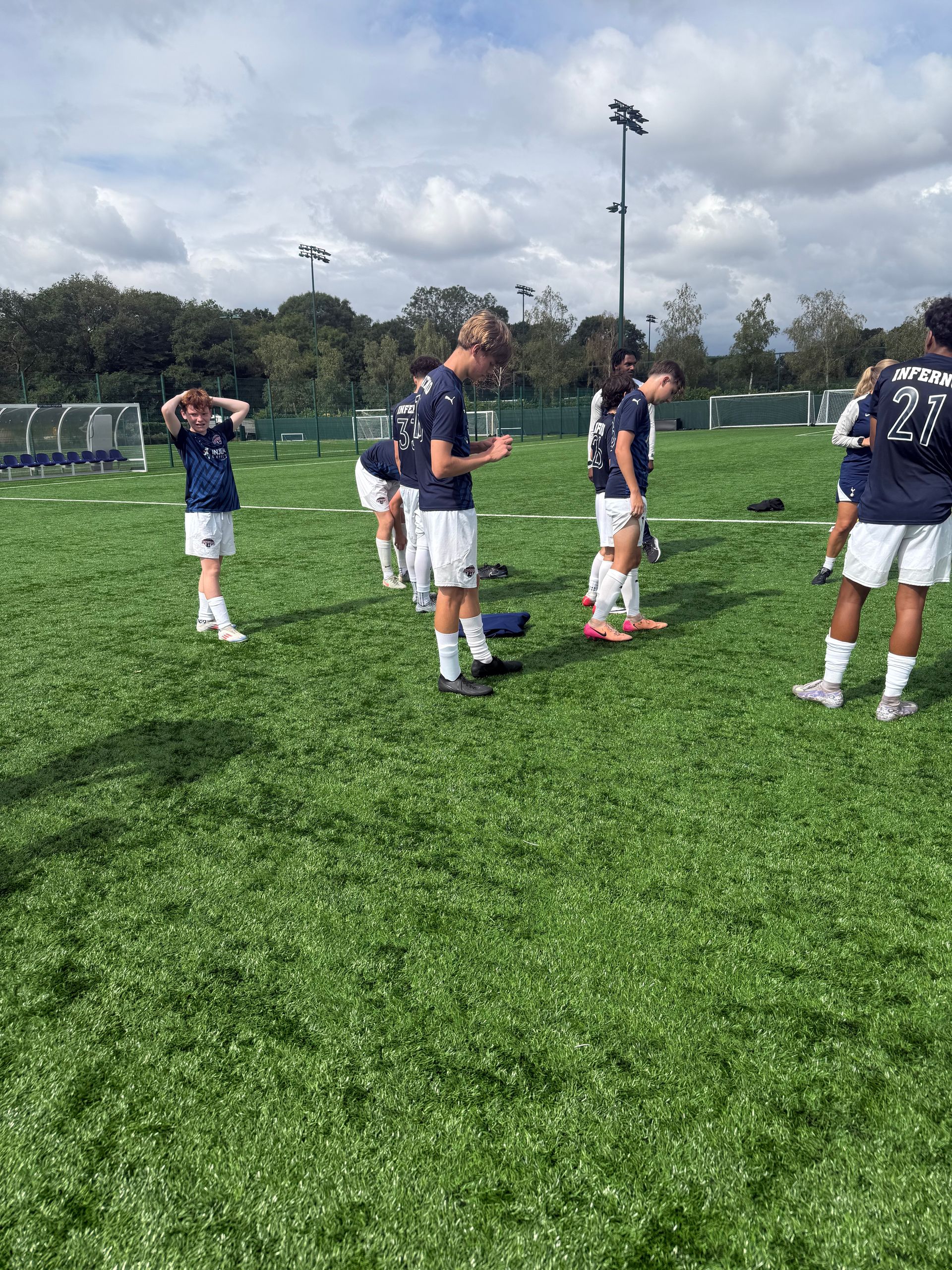 Soccer players in navy uniforms on a green field under a cloudy sky.