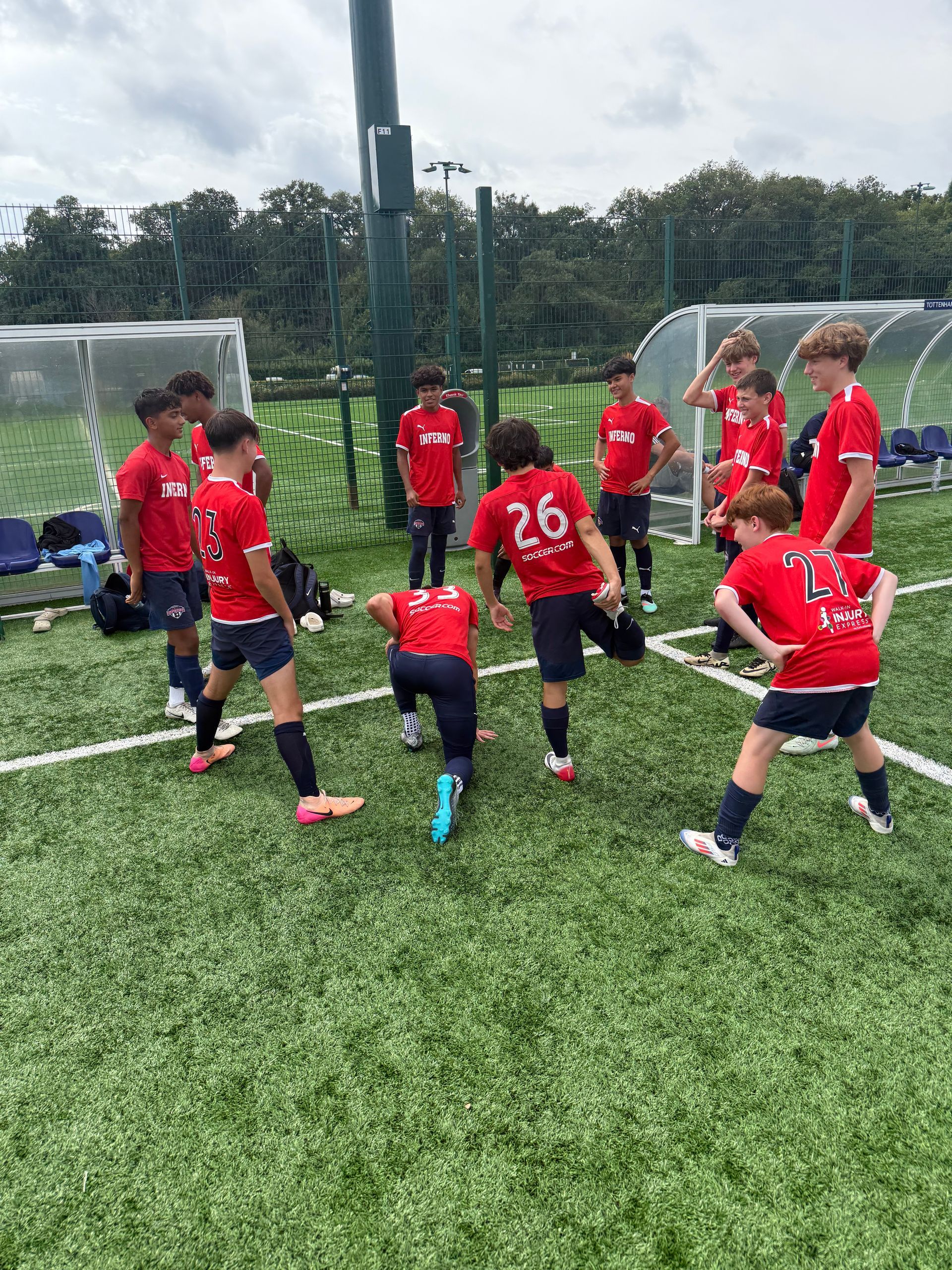 Soccer players in red jerseys stretching on a green field.
