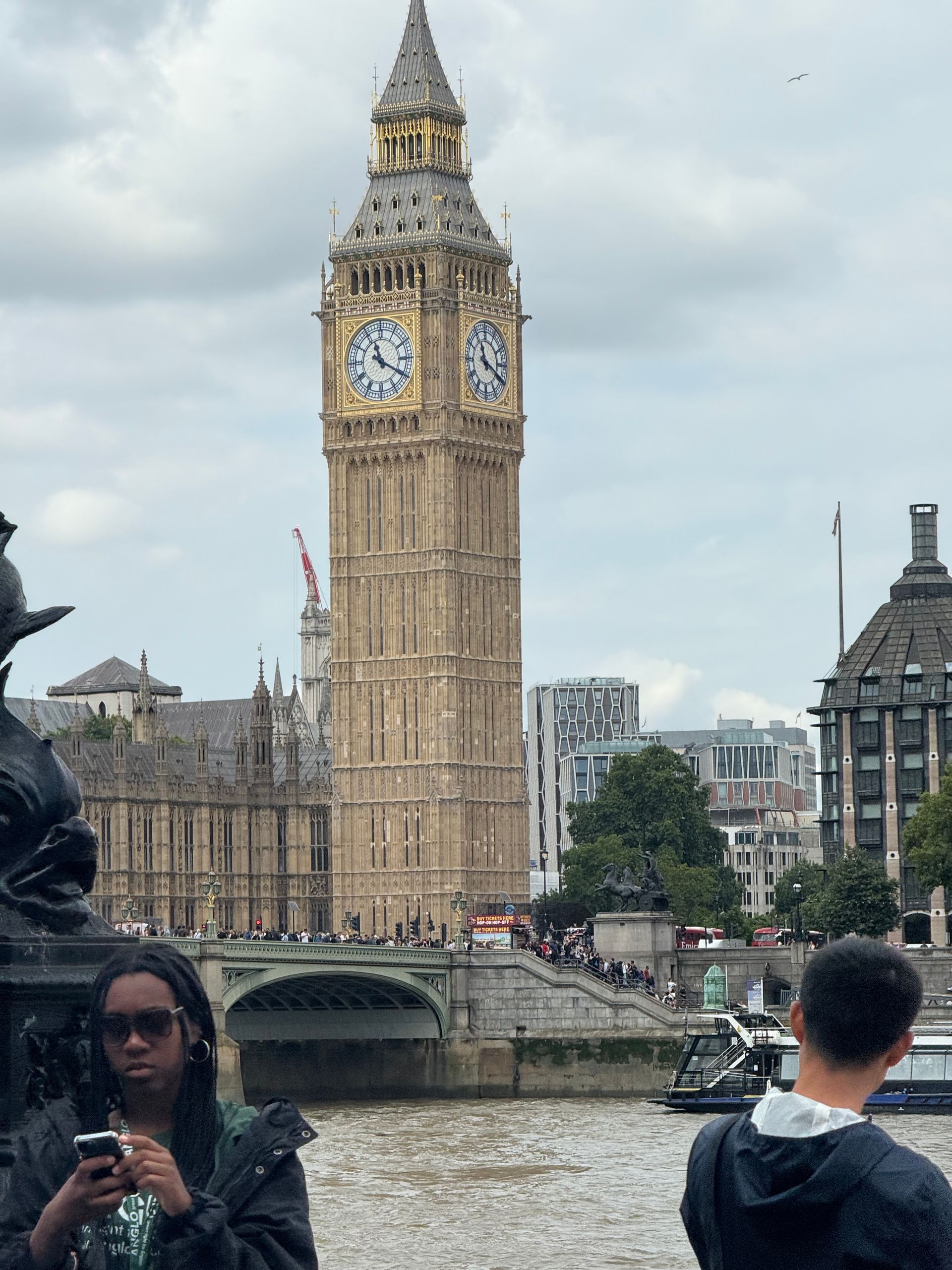 Big Ben clock tower in London, seen from across the river, with people on the bridge and in the foreground.