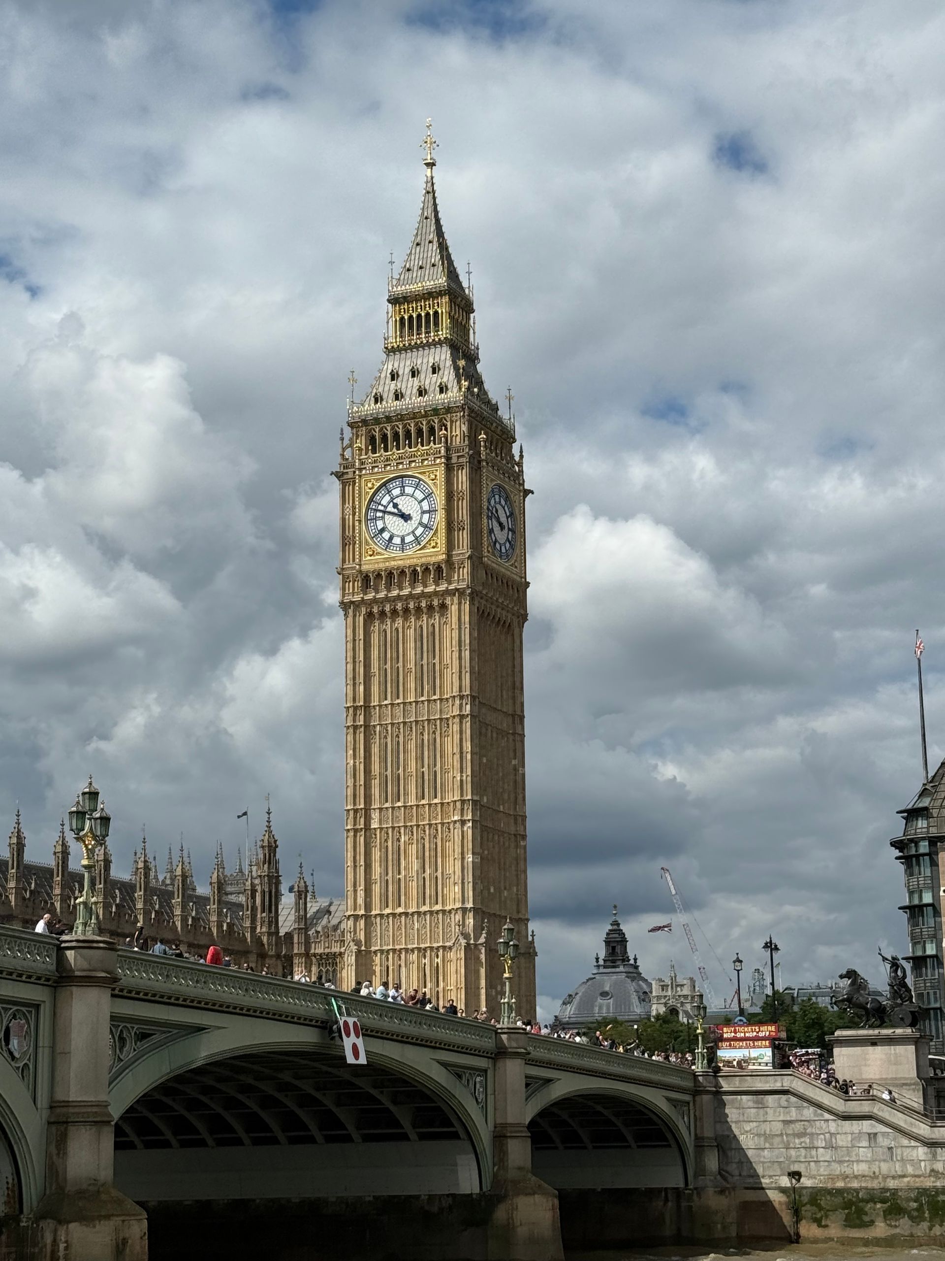 Big Ben clock tower against a cloudy sky, with a bridge in the foreground.