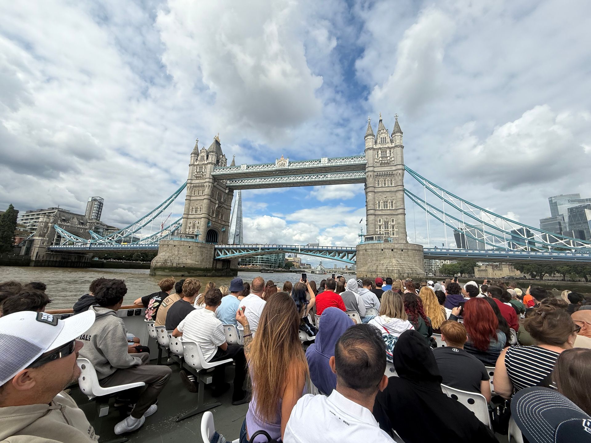 People on a boat viewing Tower Bridge, London. Blue sky, cloudy.