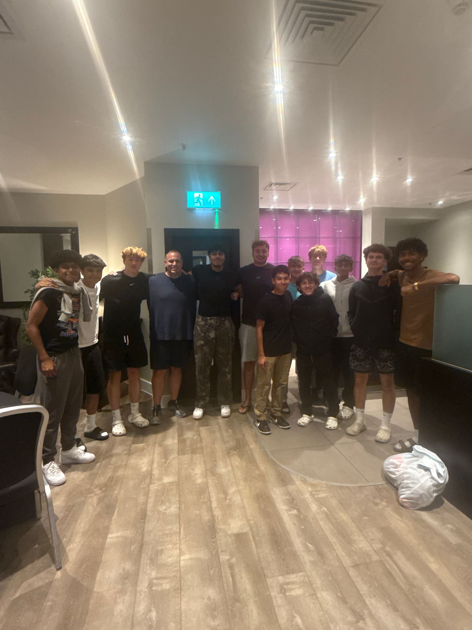 Group of men and boys pose together indoors; some have arms around each other.