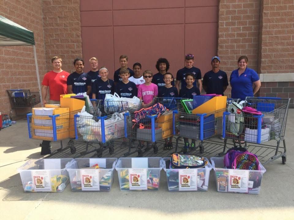 Group poses with full shopping carts and bins of supplies outside a store.