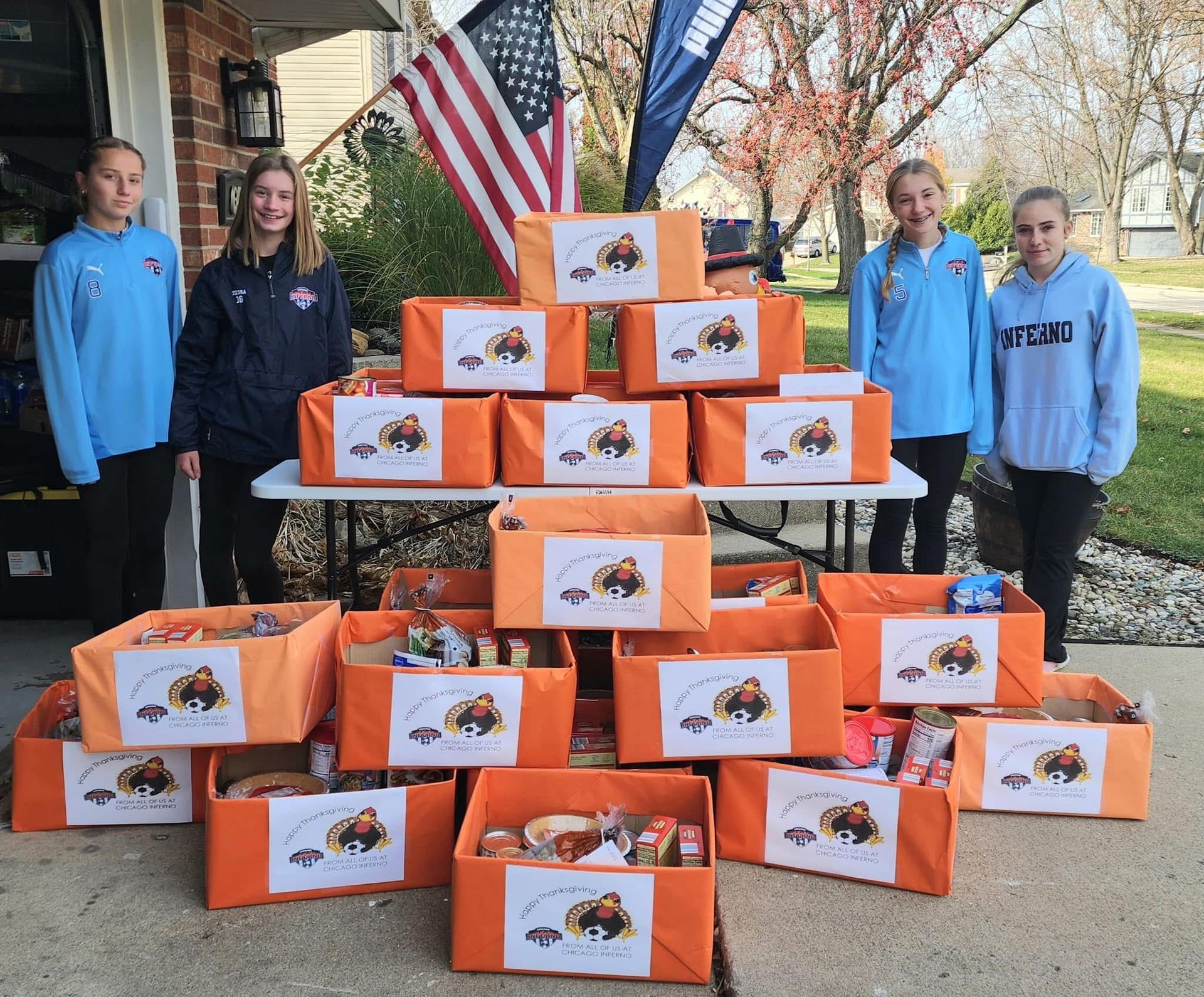 Five girls stand with many orange boxes filled with goods in front of a house, possibly for donation.  this was for the Thanksgiving fundraiser