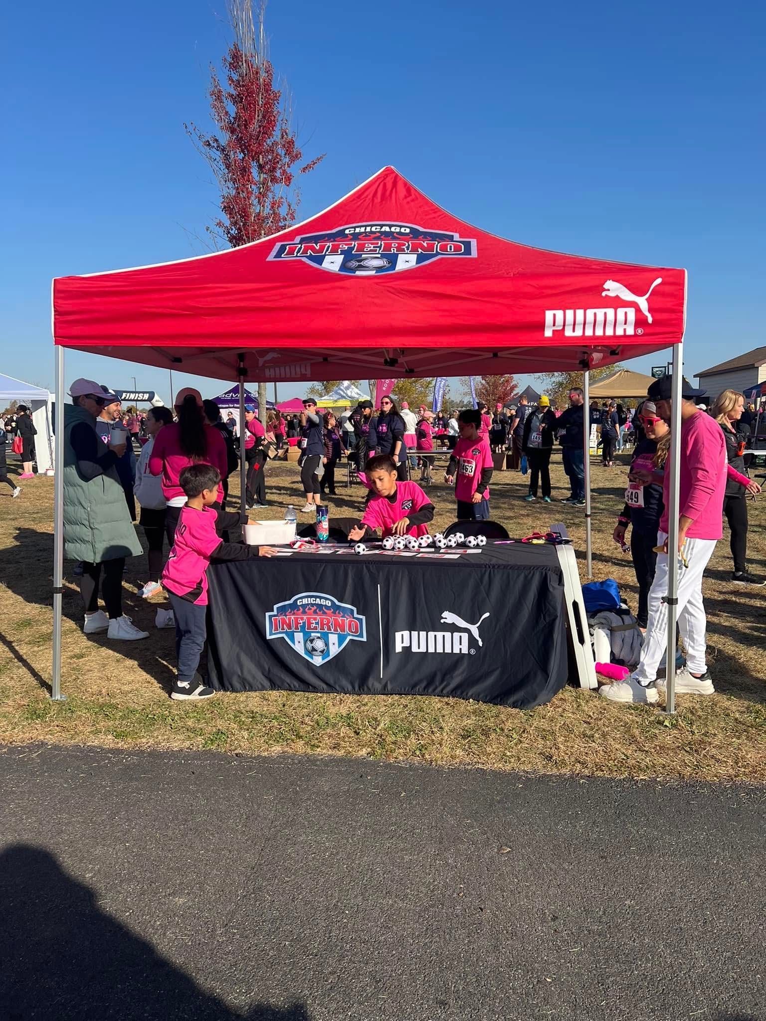 Red Puma tent with a table selling soccer merchandise, outdoor event.