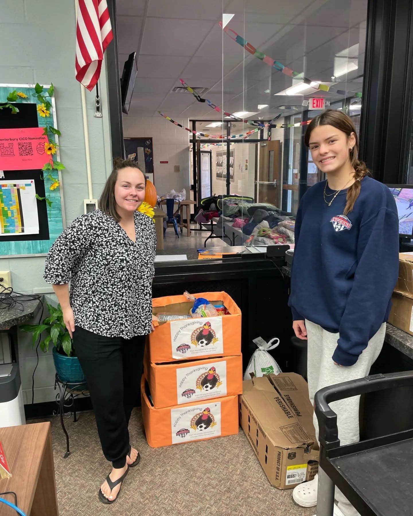 Two people stand near stacked donation boxes in a classroom.
