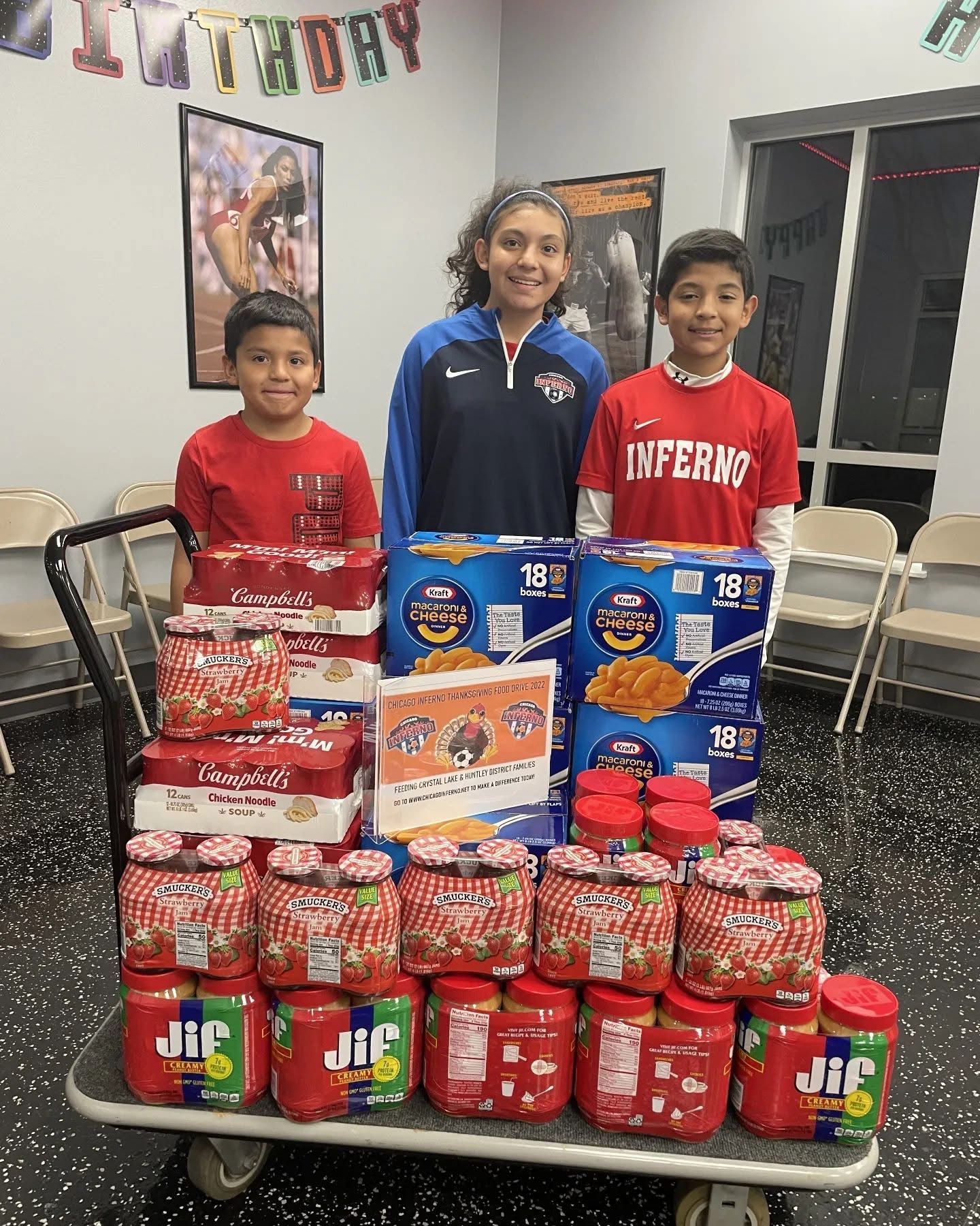 Three children stand behind a cart piled high with food donations.